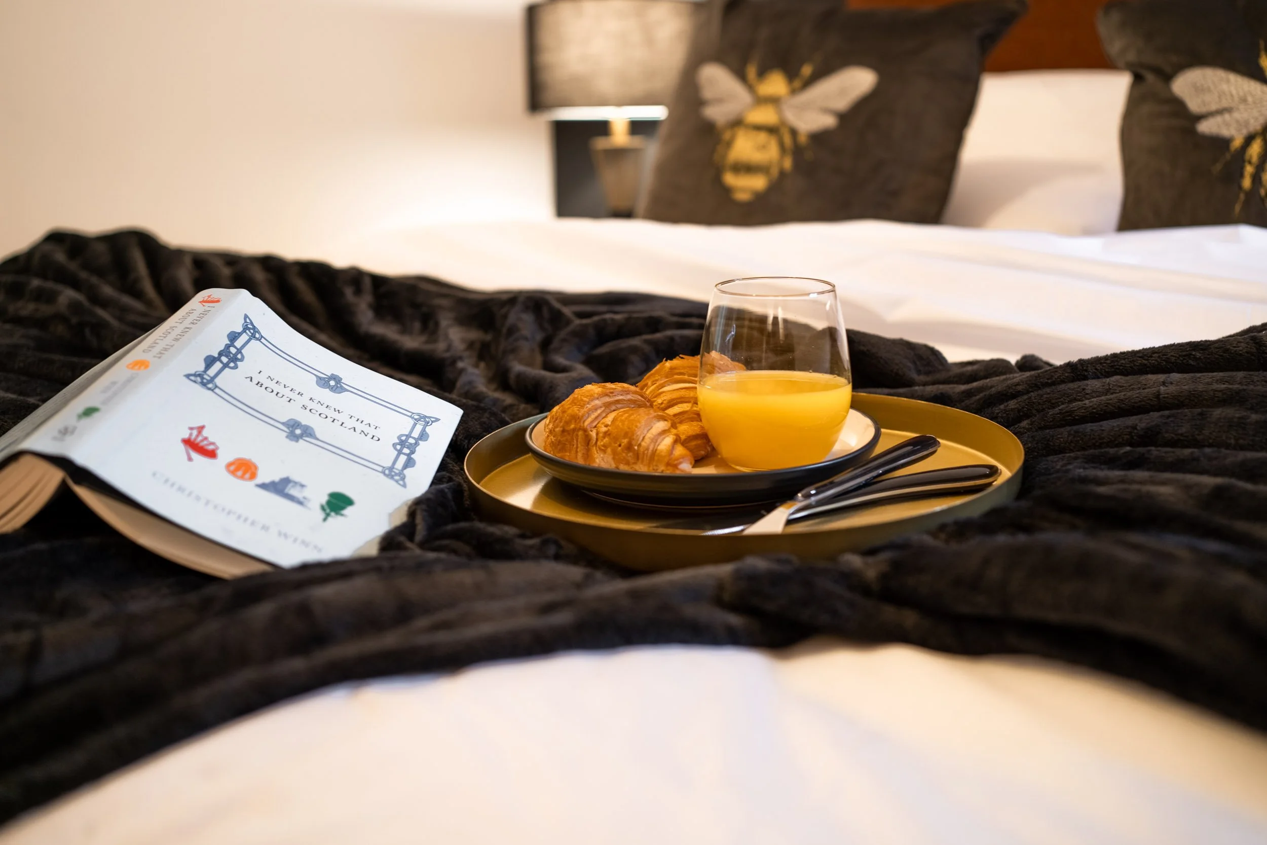 Breakfast tray with croissants and orange juice placed on a bed in a hotel room.