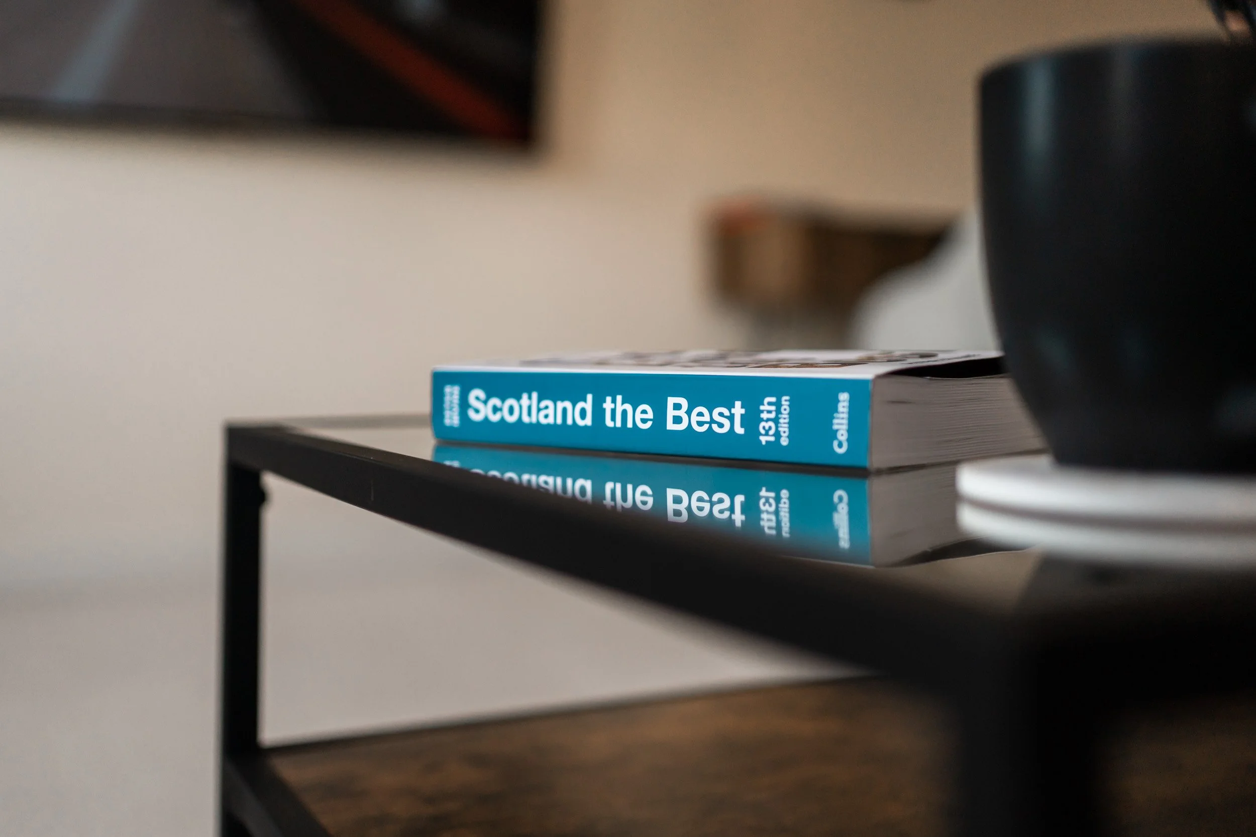 Close-up of a travel guidebook titled 'Scotland the Best' lying on a black table, with a black cup partially visible on the right side of the image.