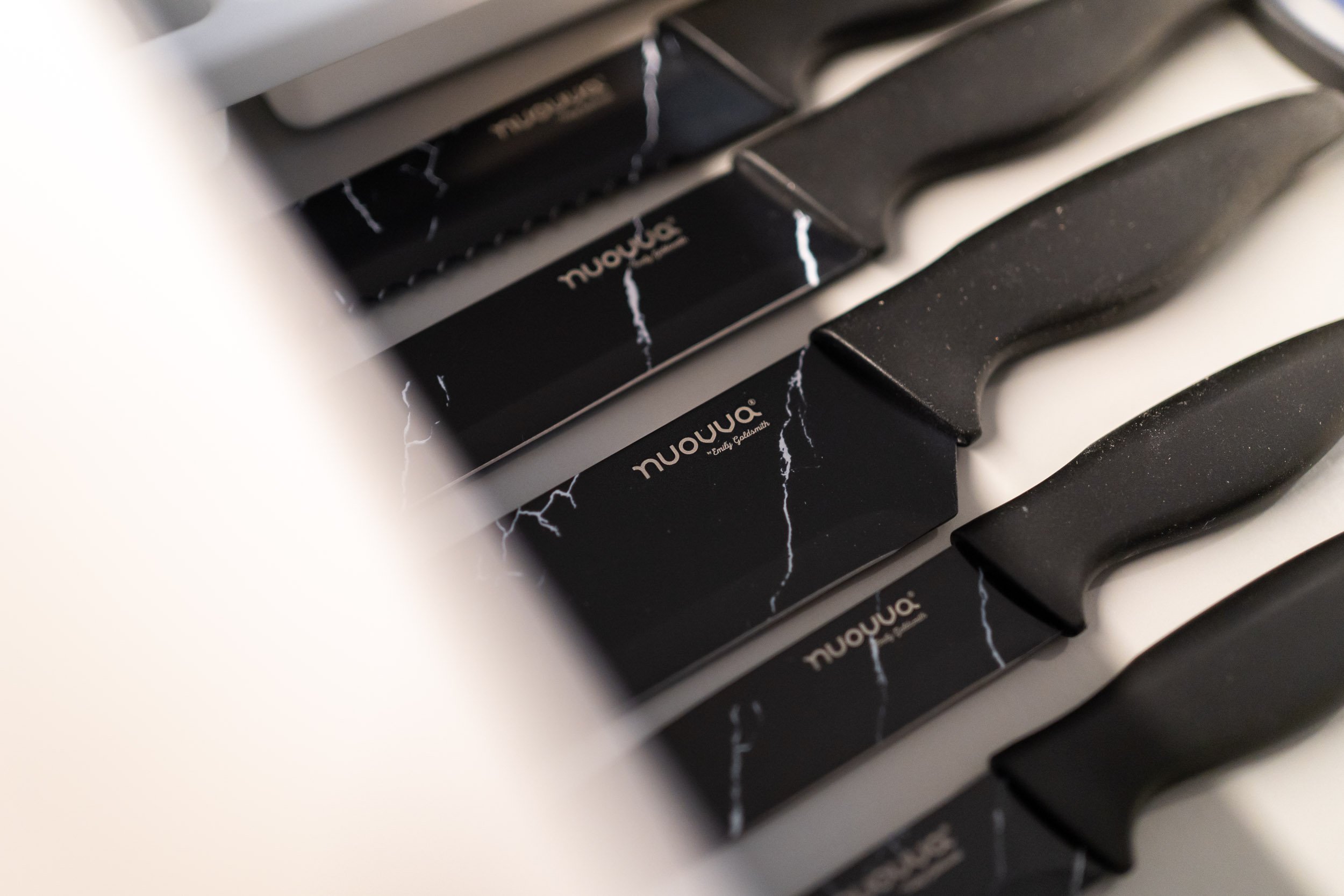 A close-up view of black knives with black handles, arranged in a row inside a drawer, with labels that read 'nuovuo' and a lightning bolt design on the packaging.