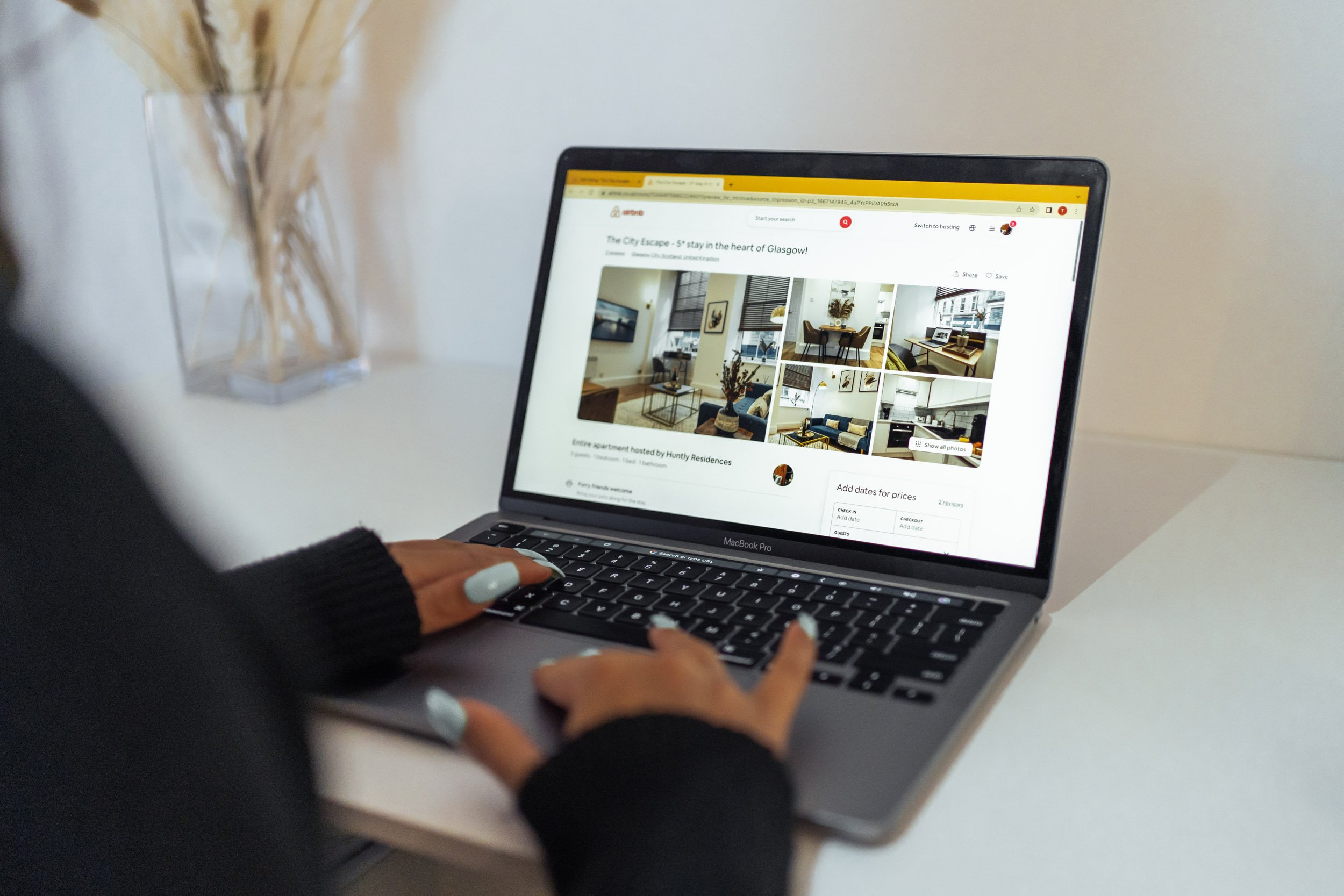 Person browsing an online apartment listing on a MacBook Pro laptop, showing photos of a modern living room.