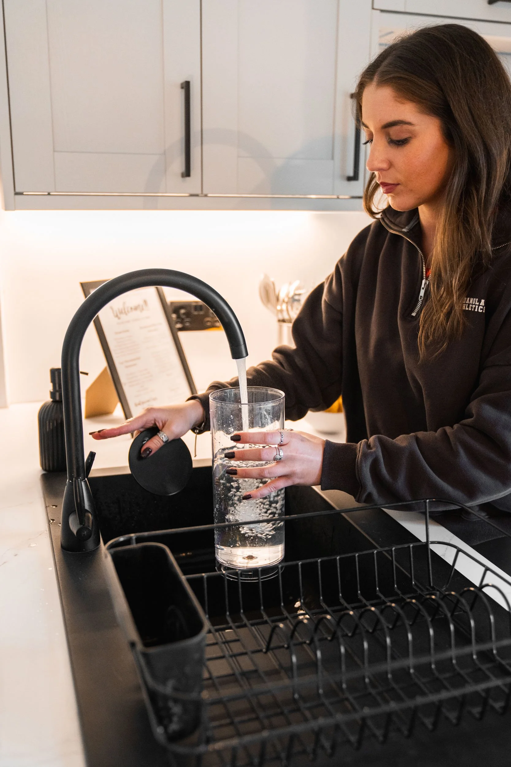 A woman washing a tall glass of water at a kitchen sink.