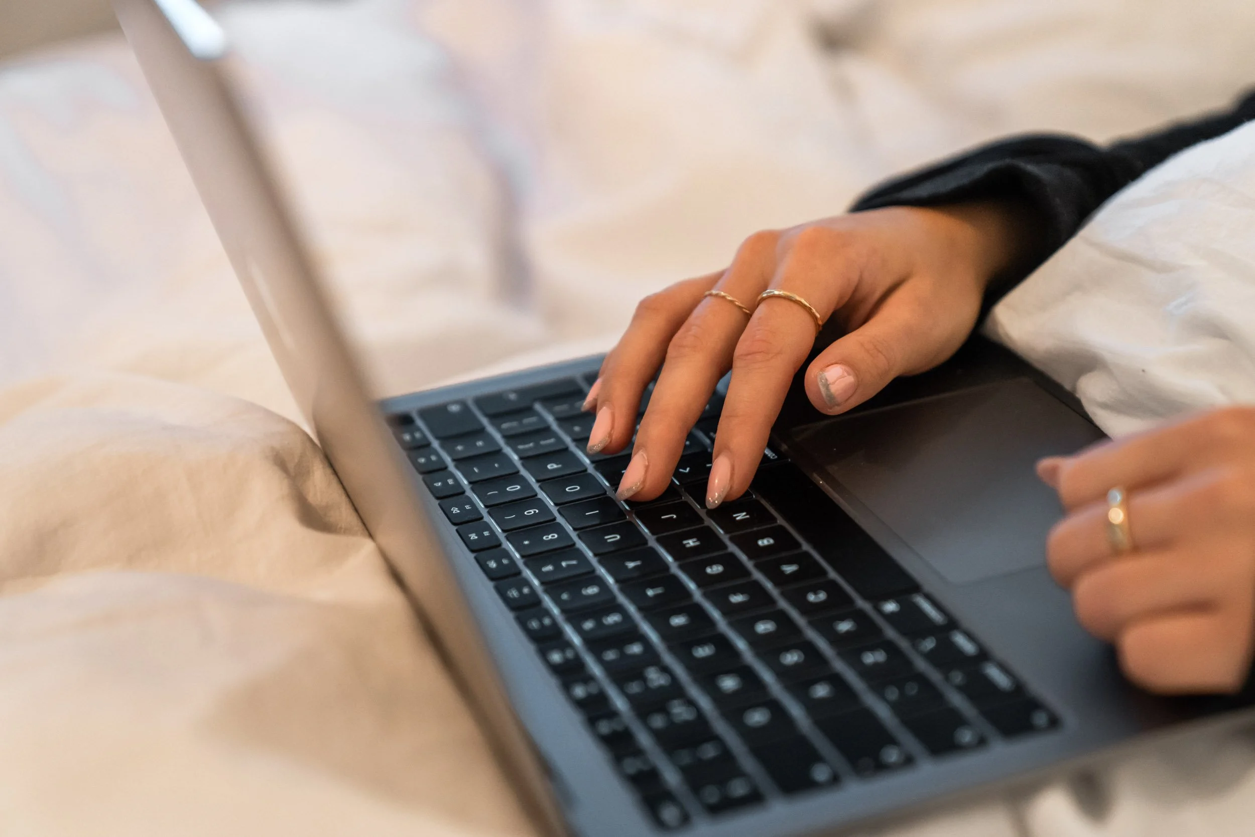 Person typing on a laptop keyboard while lying in bed.