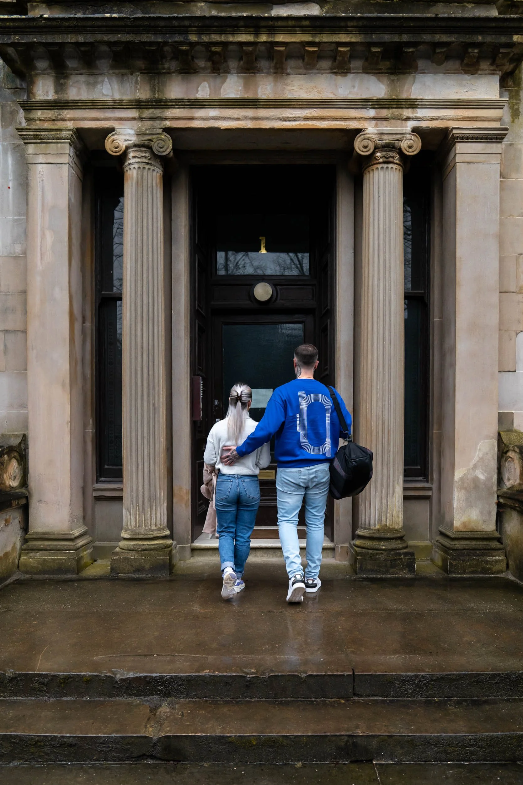 A man and woman walking into a historic building with classical columns, viewed from behind.