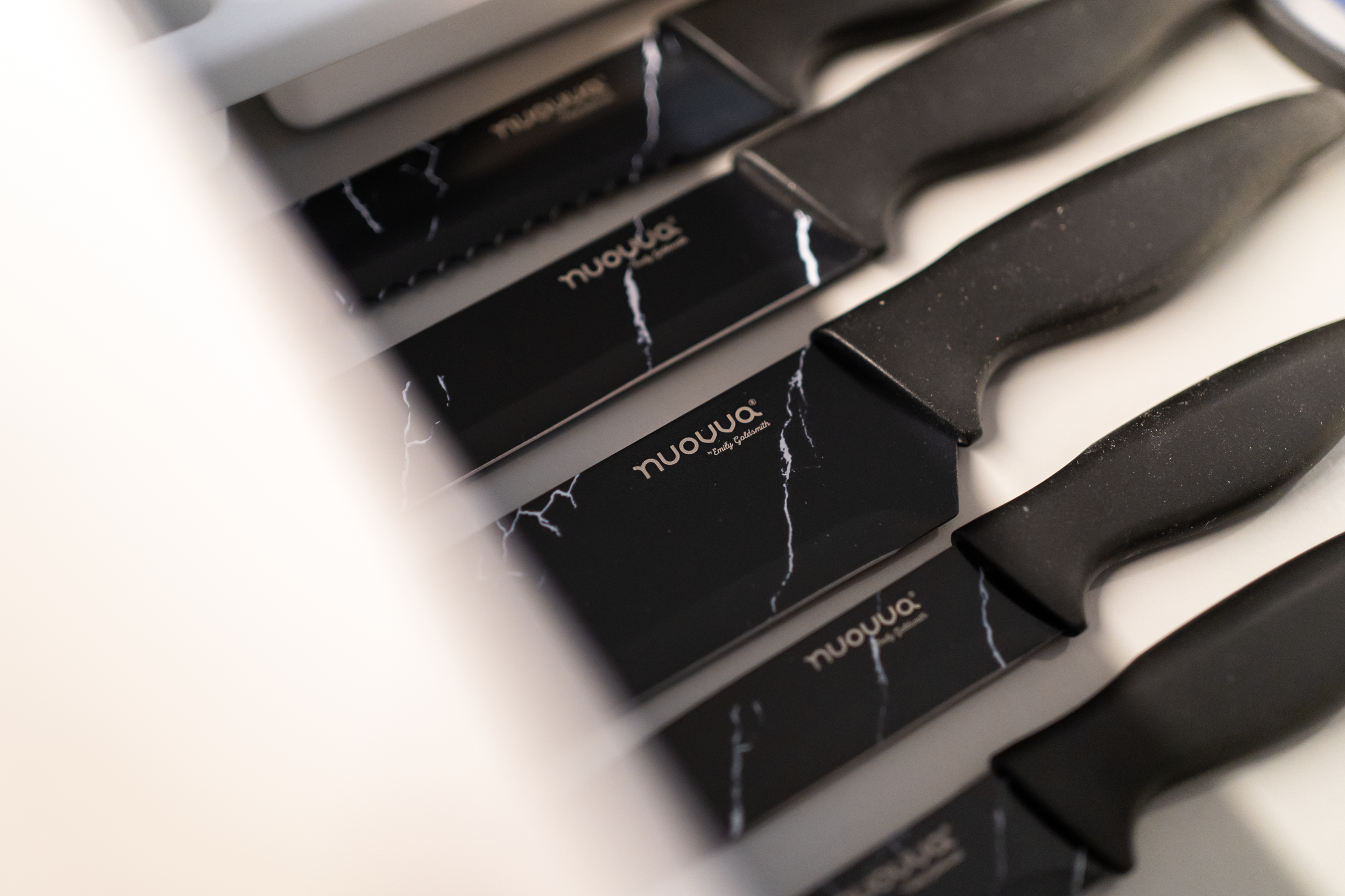 Close-up of black kitchen knives with the brand name 'NuWave' on the blades, resting on a white surface.
