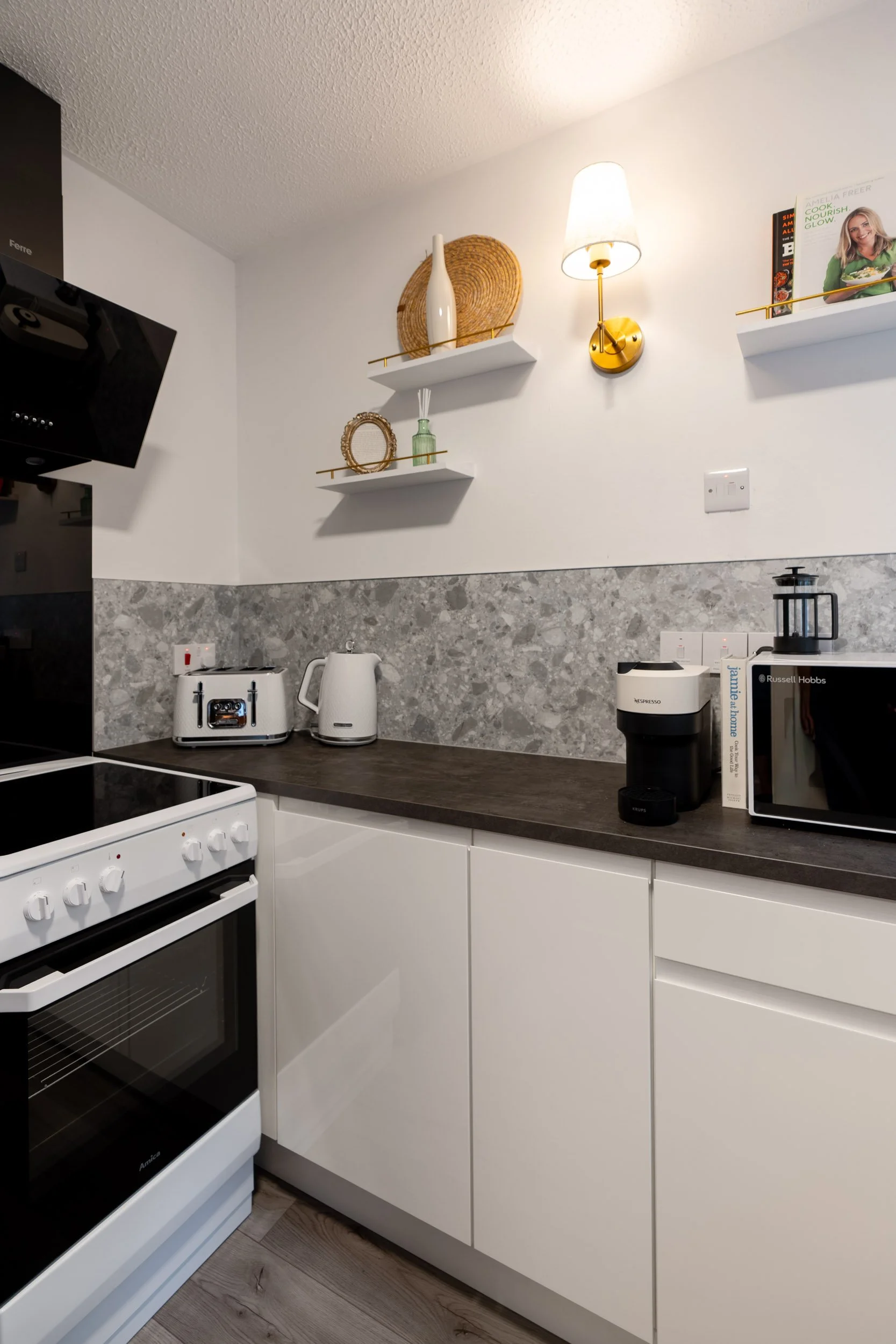 Kitchen with white cabinets, black countertop, gray backsplash, and various appliances including a toaster, kettle, coffee machine, microwave, and black extractor hood.