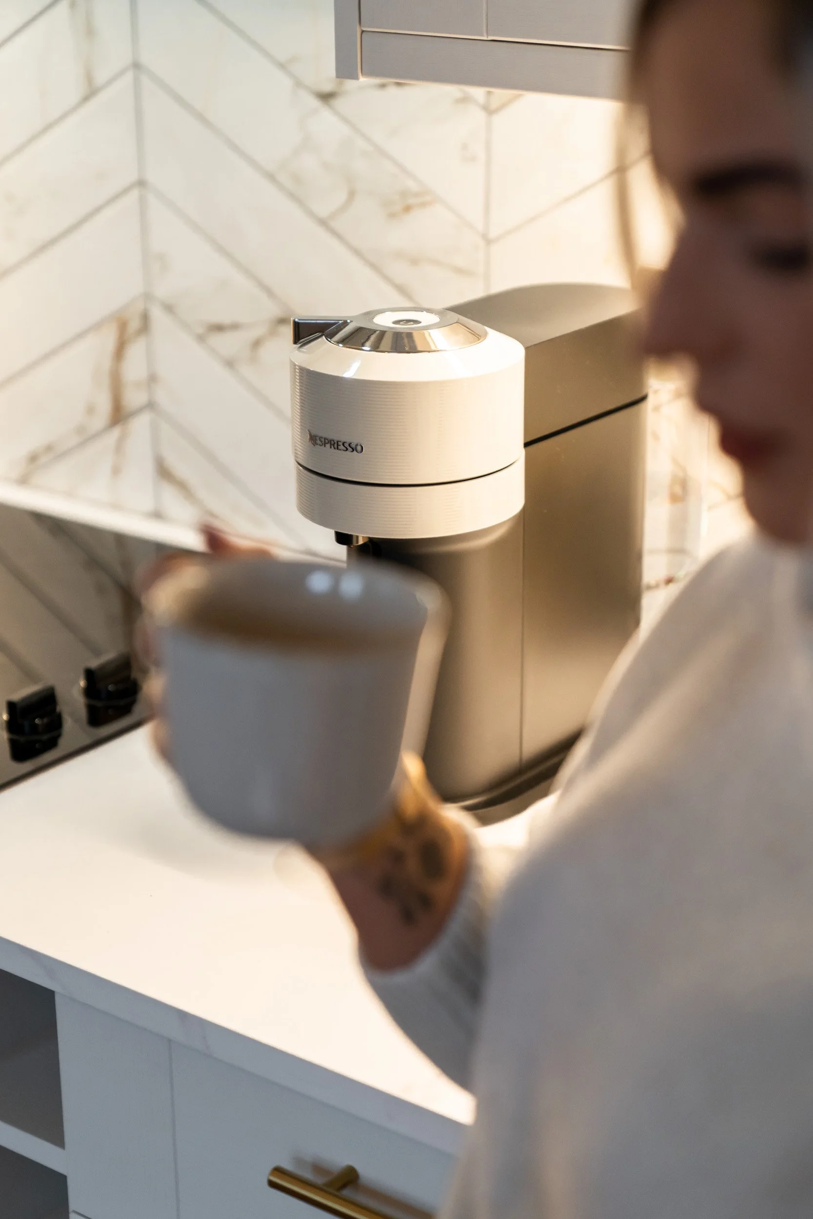 A woman holding a mug in a kitchen with a Nespresso coffee machine on the counter.