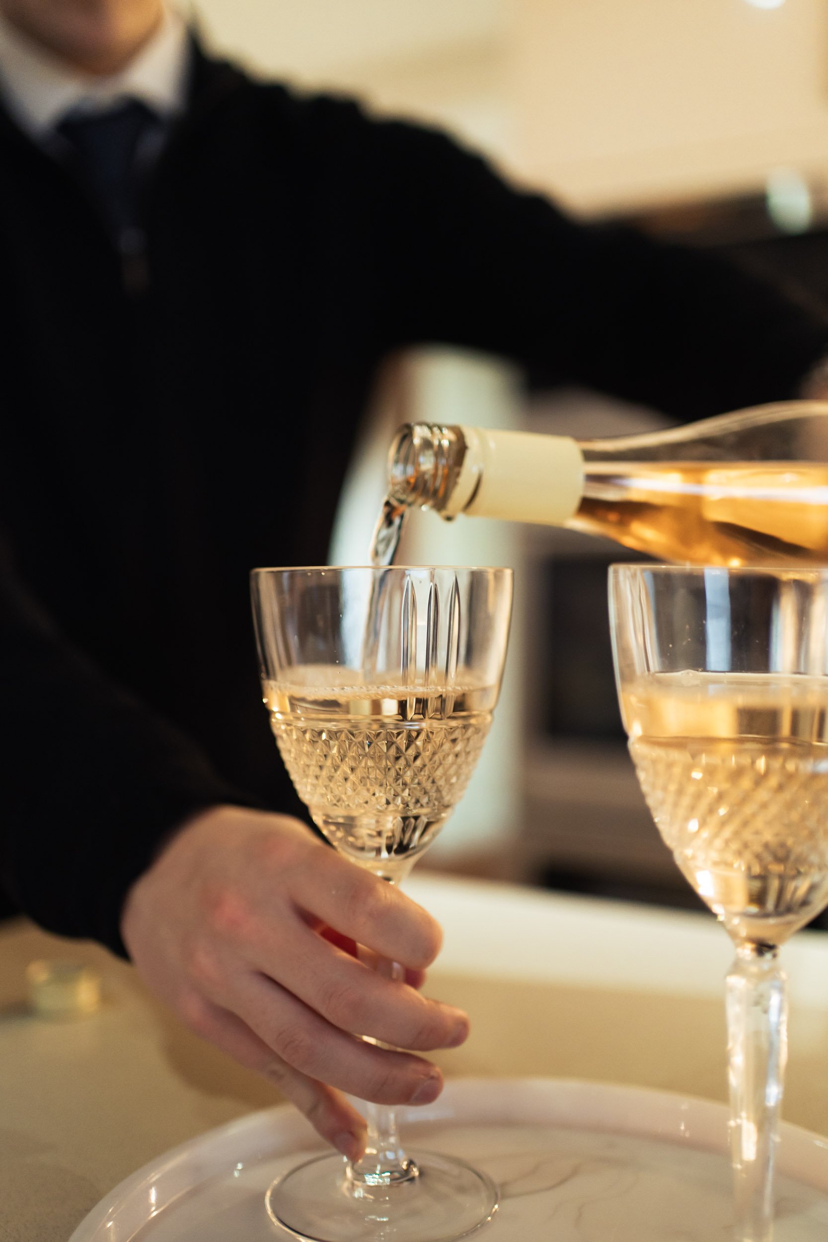Person pouring a bottle of rosé wine into a crystal glass at a table.