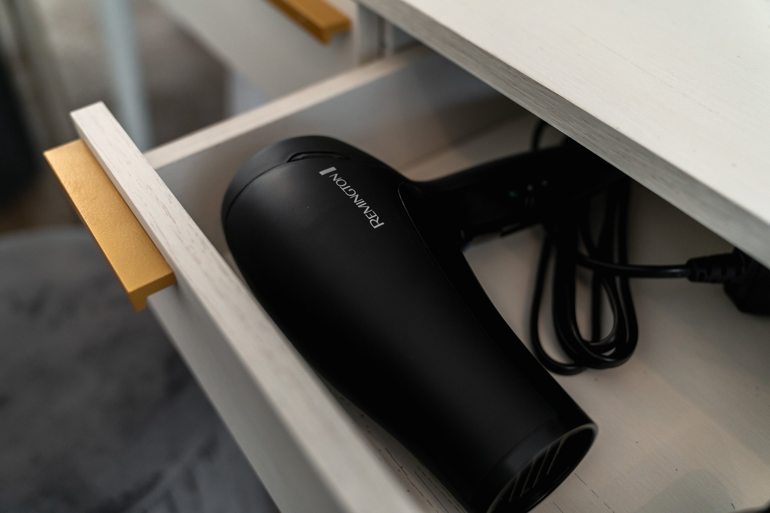 A black Remington hair dryer inside an opened drawer of a white and yellow desk.