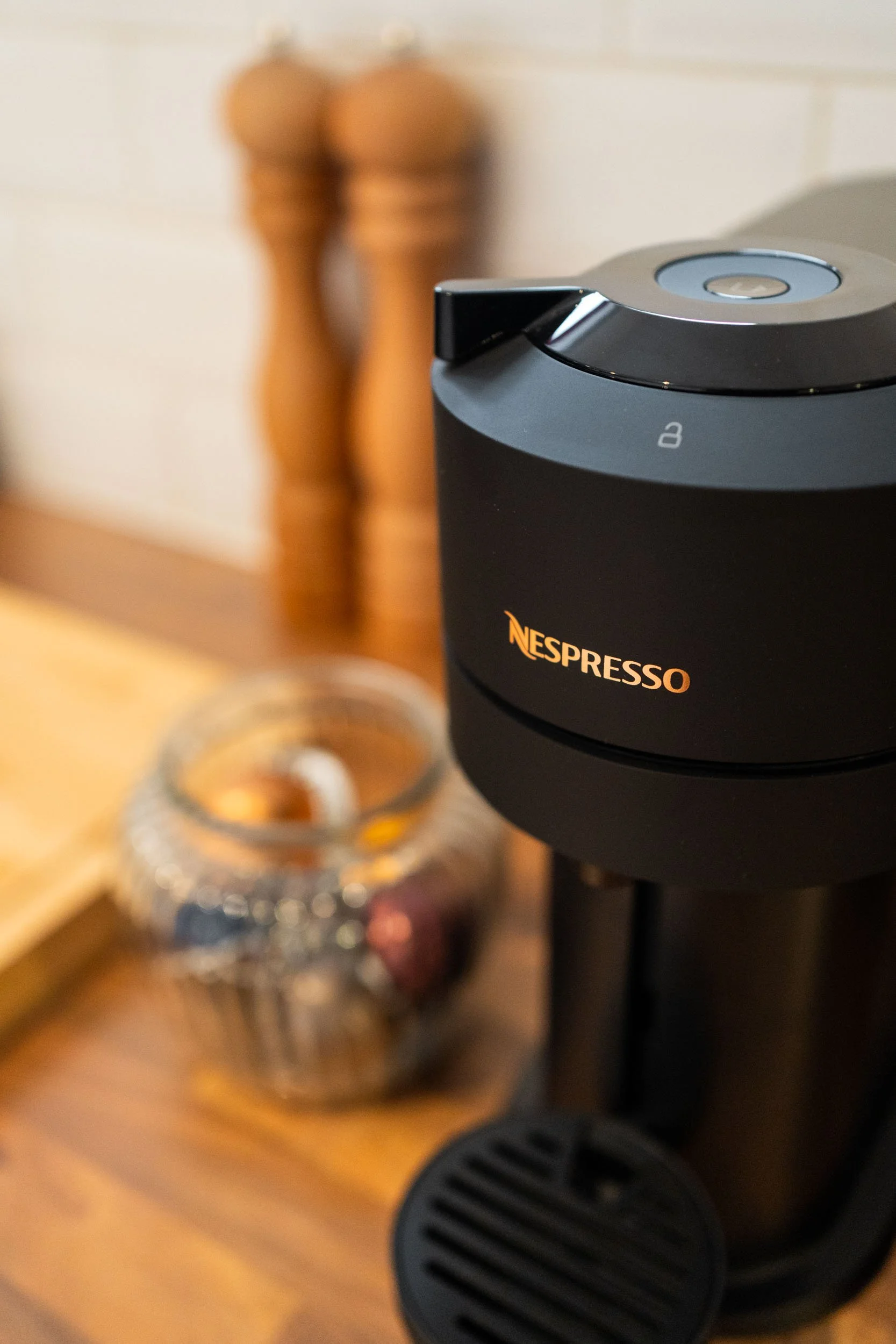 Black Nespresso coffee machine on a wooden surface with a glass jar and wooden salt and pepper shakers in the background.