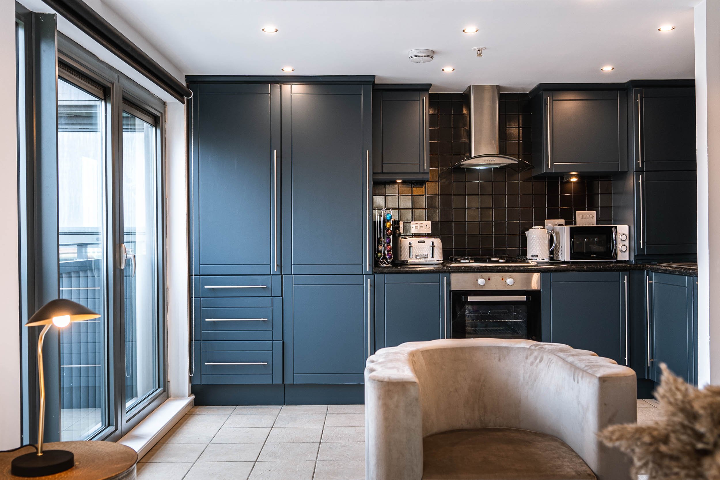 Modern kitchen with dark blue cabinets, black tile backsplash, stainless steel appliances, and a sliding glass door leading outside.