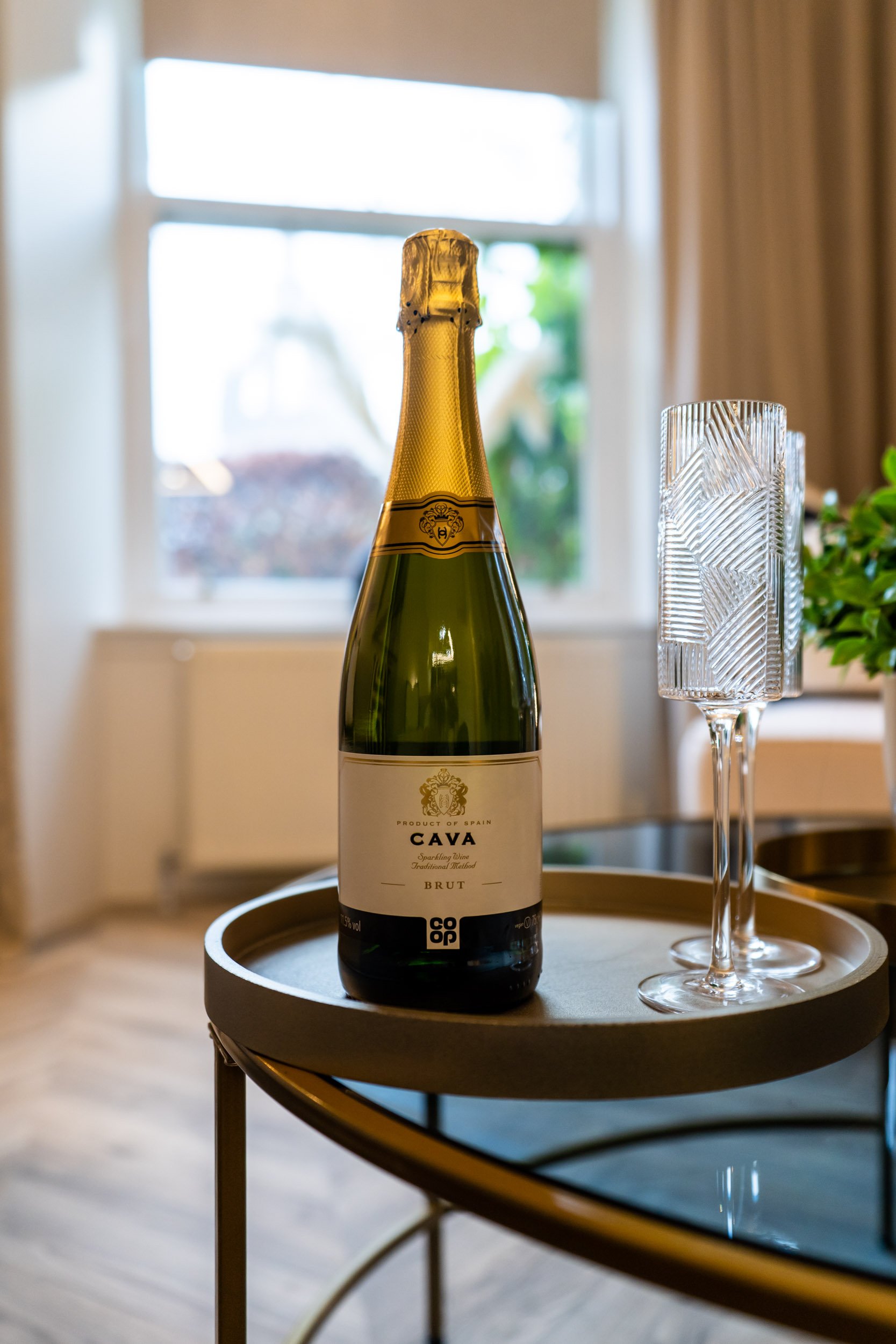 A bottle of Cava Brut sparkling wine with two empty crystal flutes on a round tray.