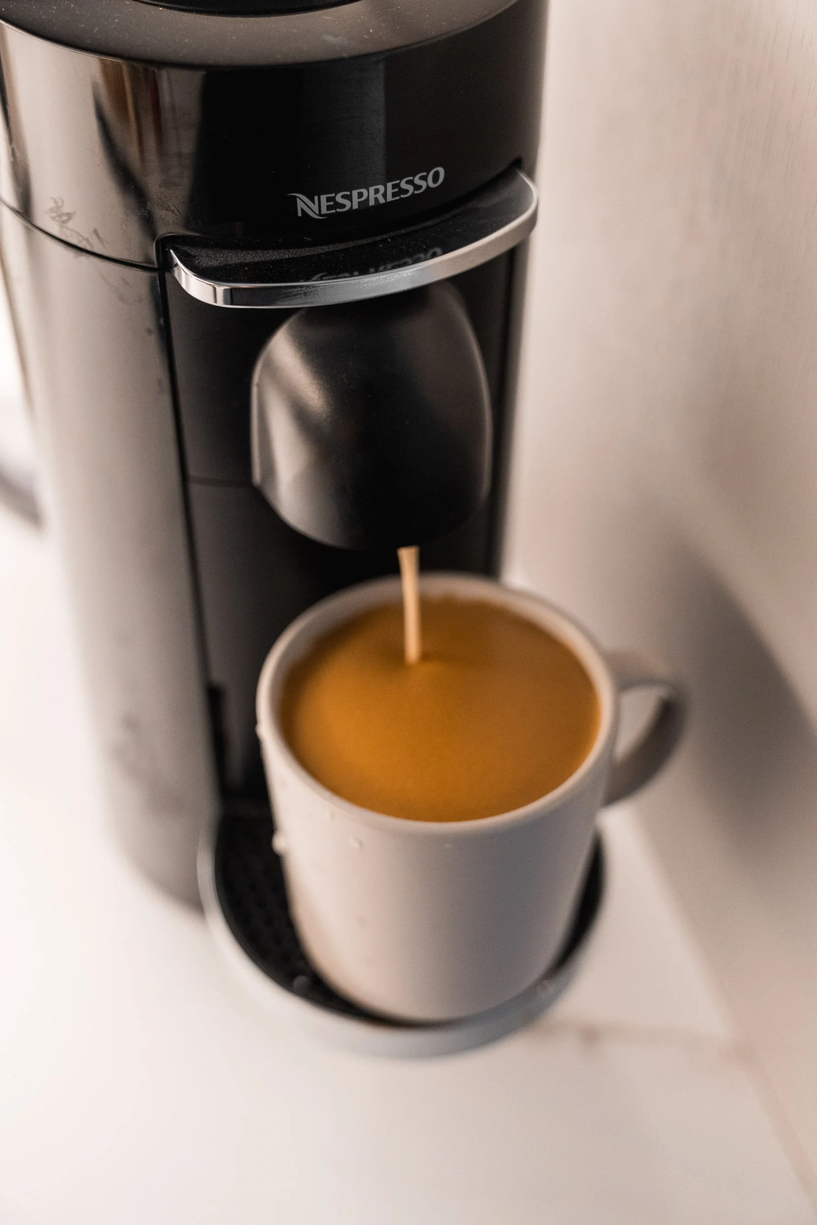 A white mug on a coffee machine drip tray with coffee dripping from the spout into the mug.