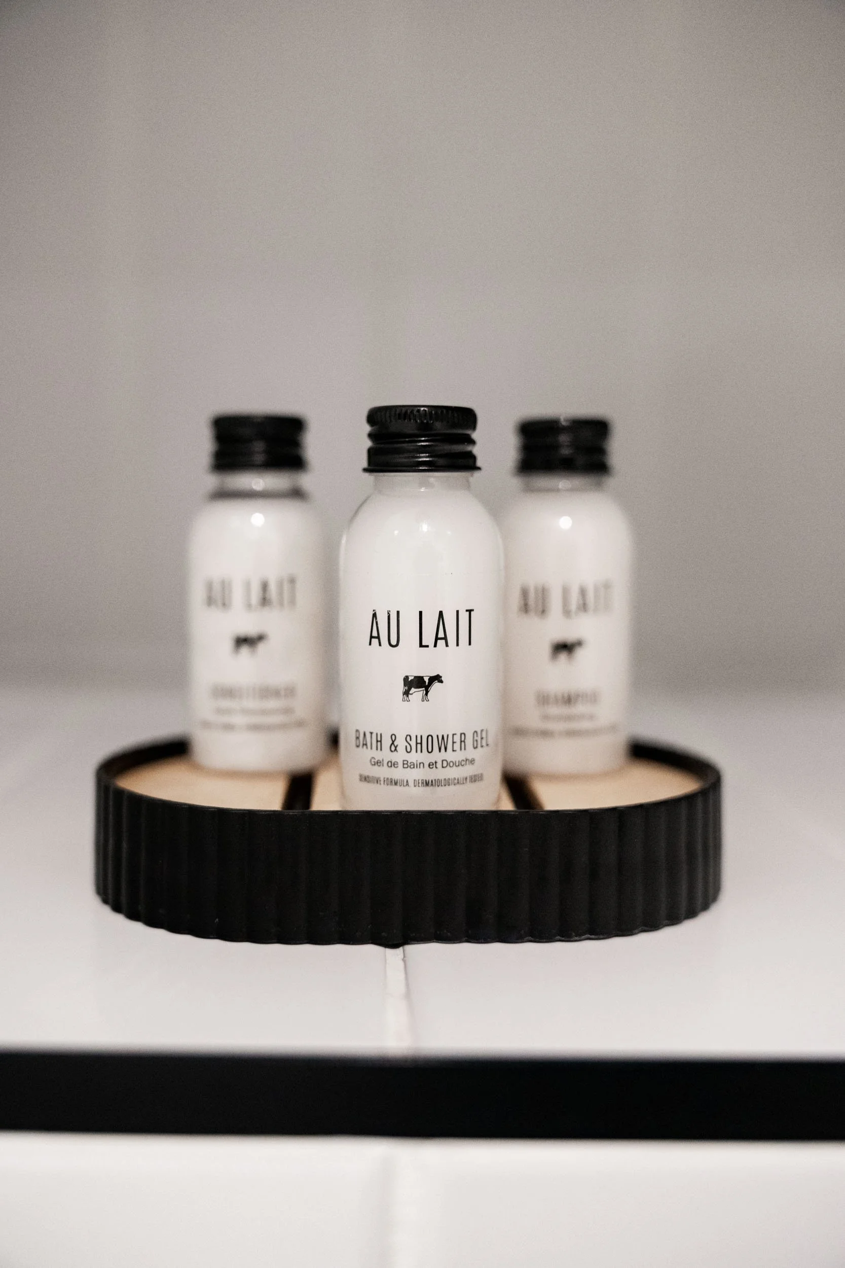 Three bottles of Au Lait bath and shower gel on a pod style black tray.