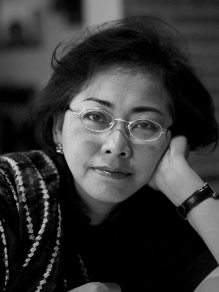 Black-and-white portrait of Restu Imansari Kusumaningrum, Hypatia Co-Founder and Director of Research and Community Outreach, resting her chin on her hand, wearing glasses and a patterned cardigan.
