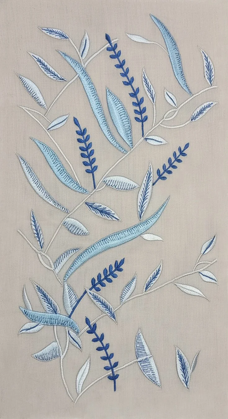 Close-up of Hypatia Sulam embroidery: navy and pale blue leaf and branch motifs hand-embroidered onto beige fabric.
