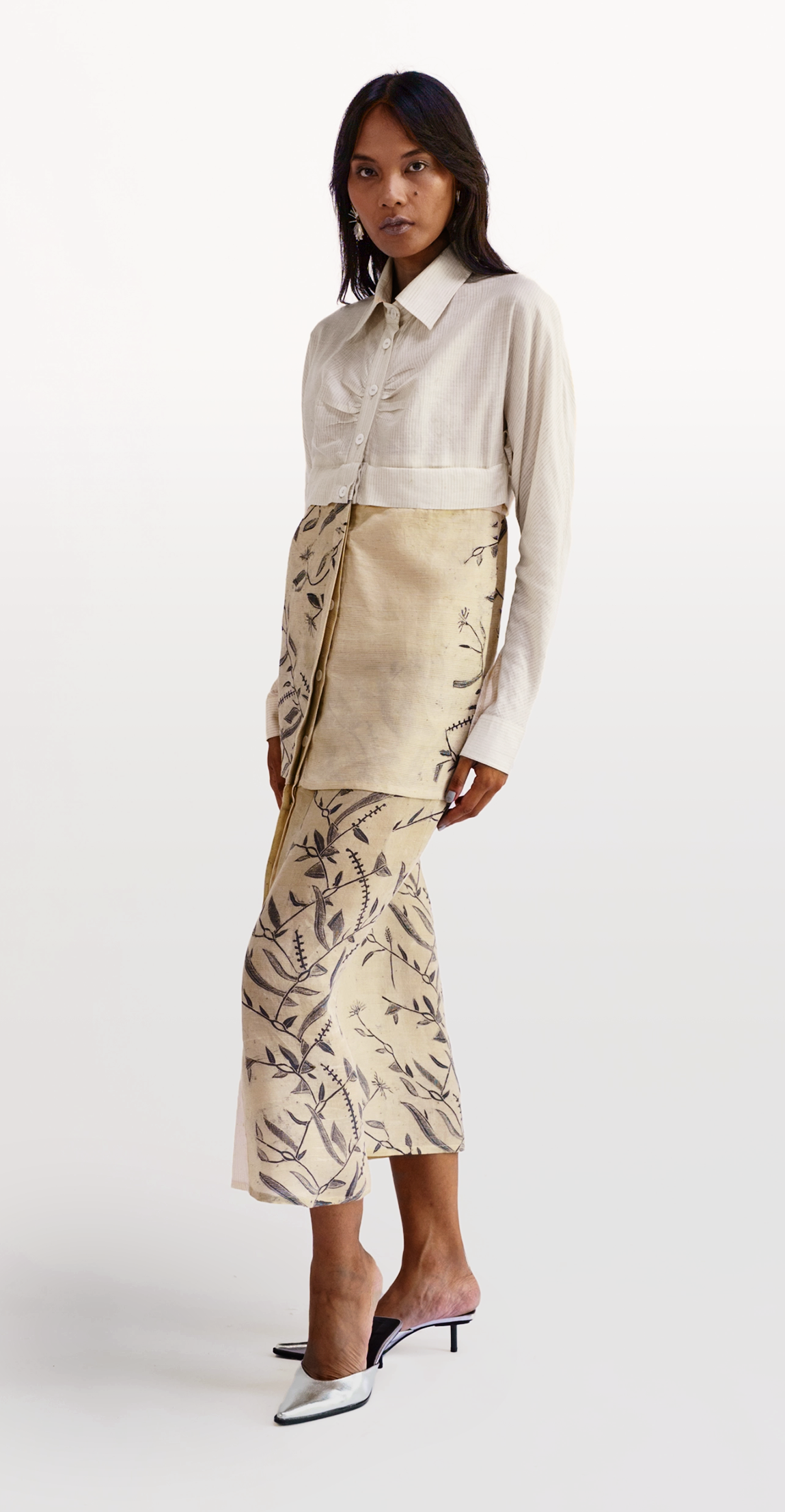 Woman wearing a cream ribbed cropped shirt layered over a long hand-painted skirt with a black botanical vine and stitch motif, from Hypatia's Combinables collection.