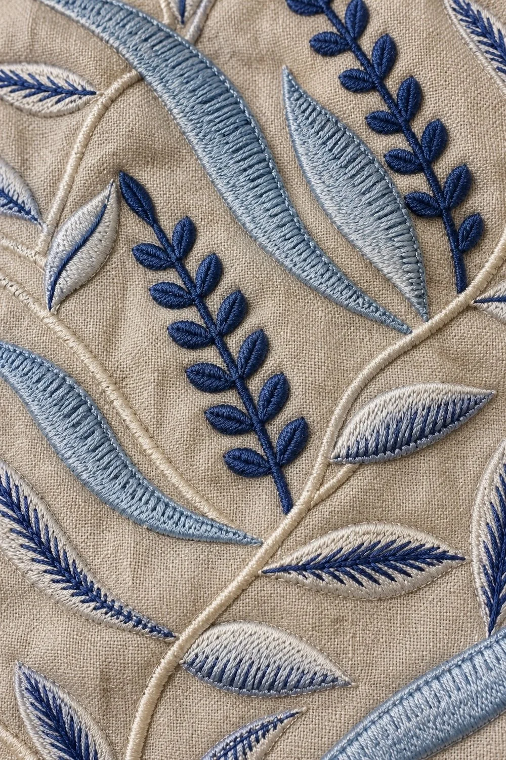 Close-up of a finished Hypatia Serat piece in beige linen, its blue and navy leaf-and- vine motif worked directly onto the material in Sulam Mesin, after the cloth had already been given its colour.
