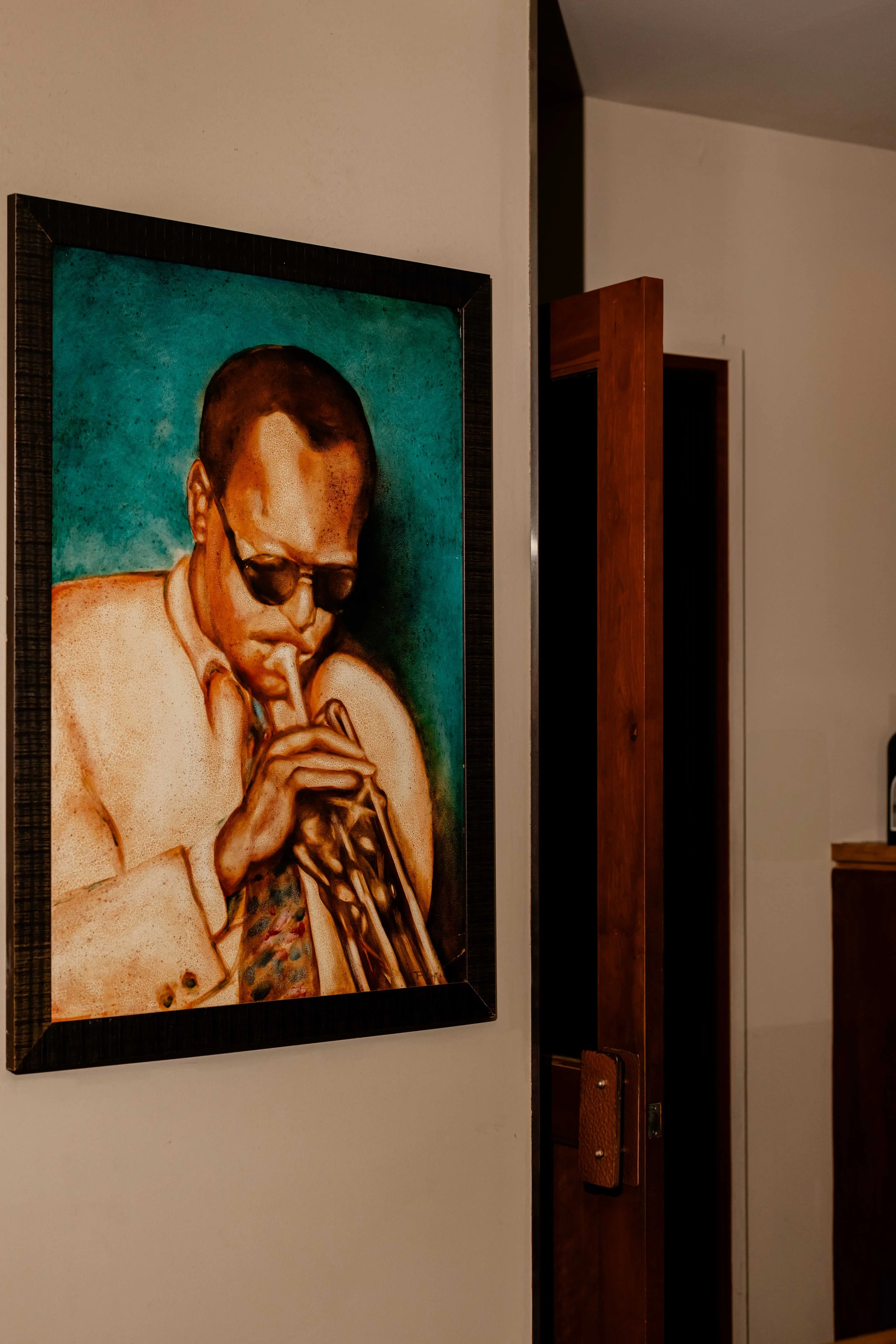 A painting of a man playing a trumpet, wearing sunglasses and a cream-colored jacket, with a teal background.