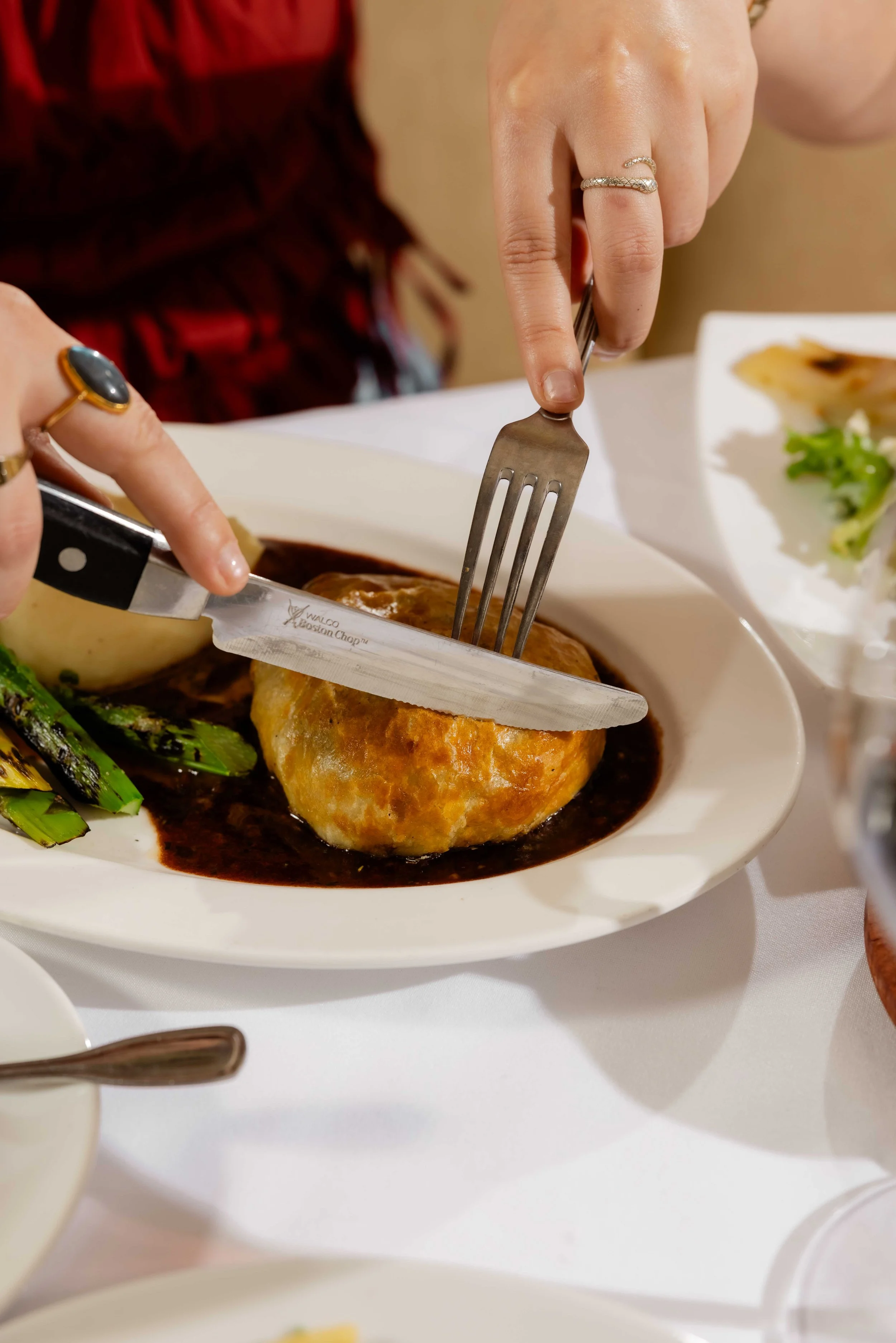 Person cutting into a beef wellington accompanied with cheddar whipped mashed potatoes and sauce, with vegetables on the side.