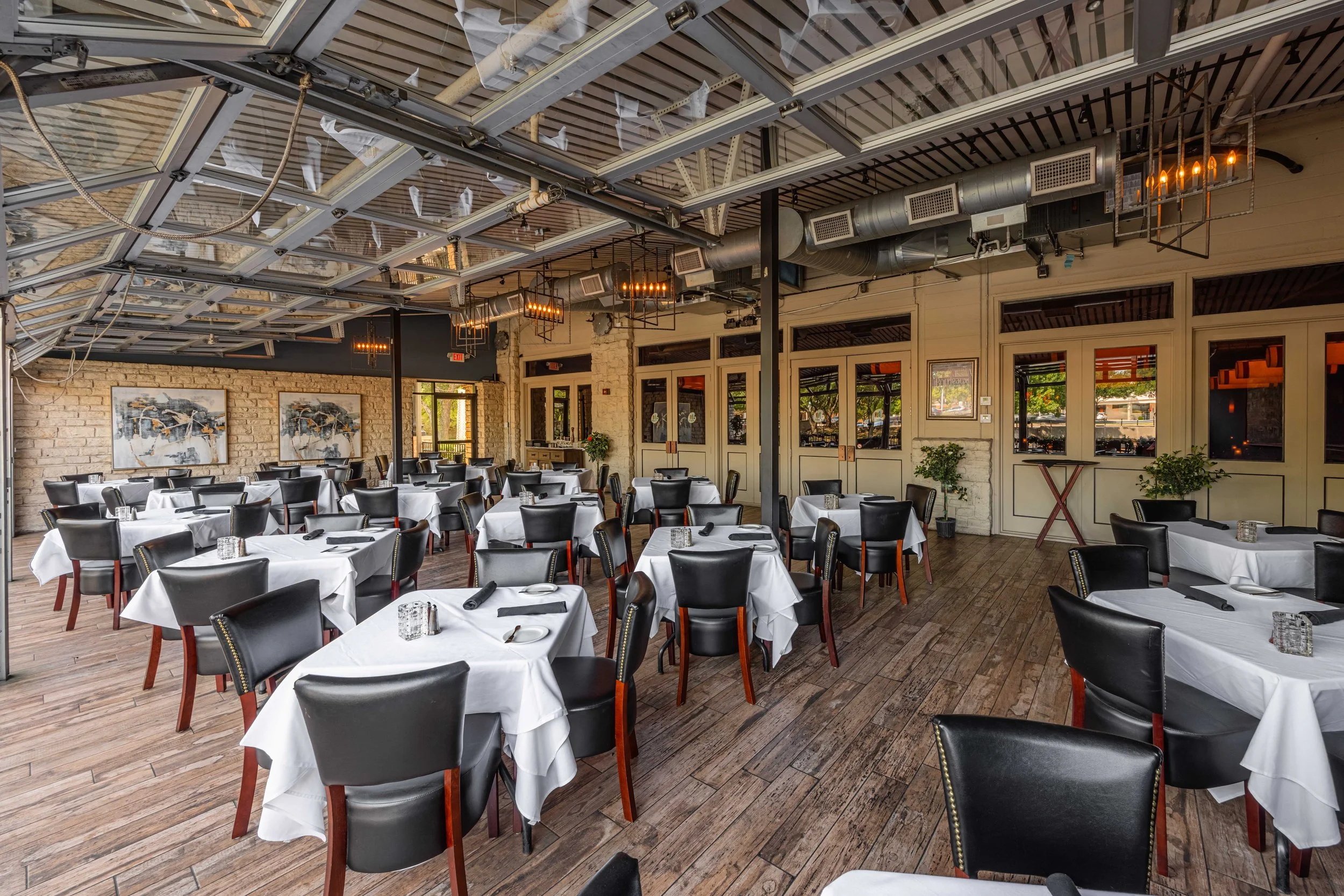 Upscale restaurant with white tablecloths, black chairs, and a rustic interior with exposed brick walls and large windows.