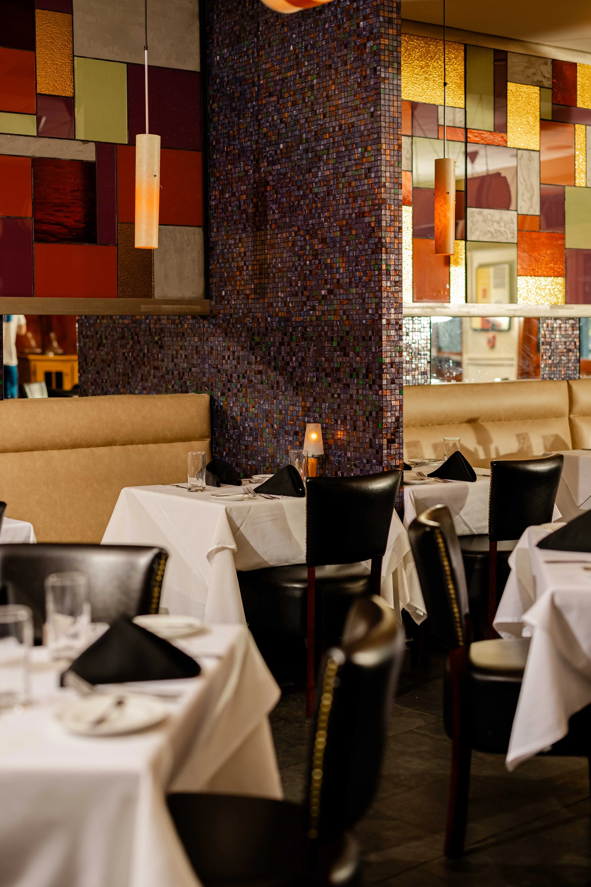 Elegant restaurant dining area with white tablecloths, black napkins, and black chairs, decorated with pendant lights and mosaic partitions.
