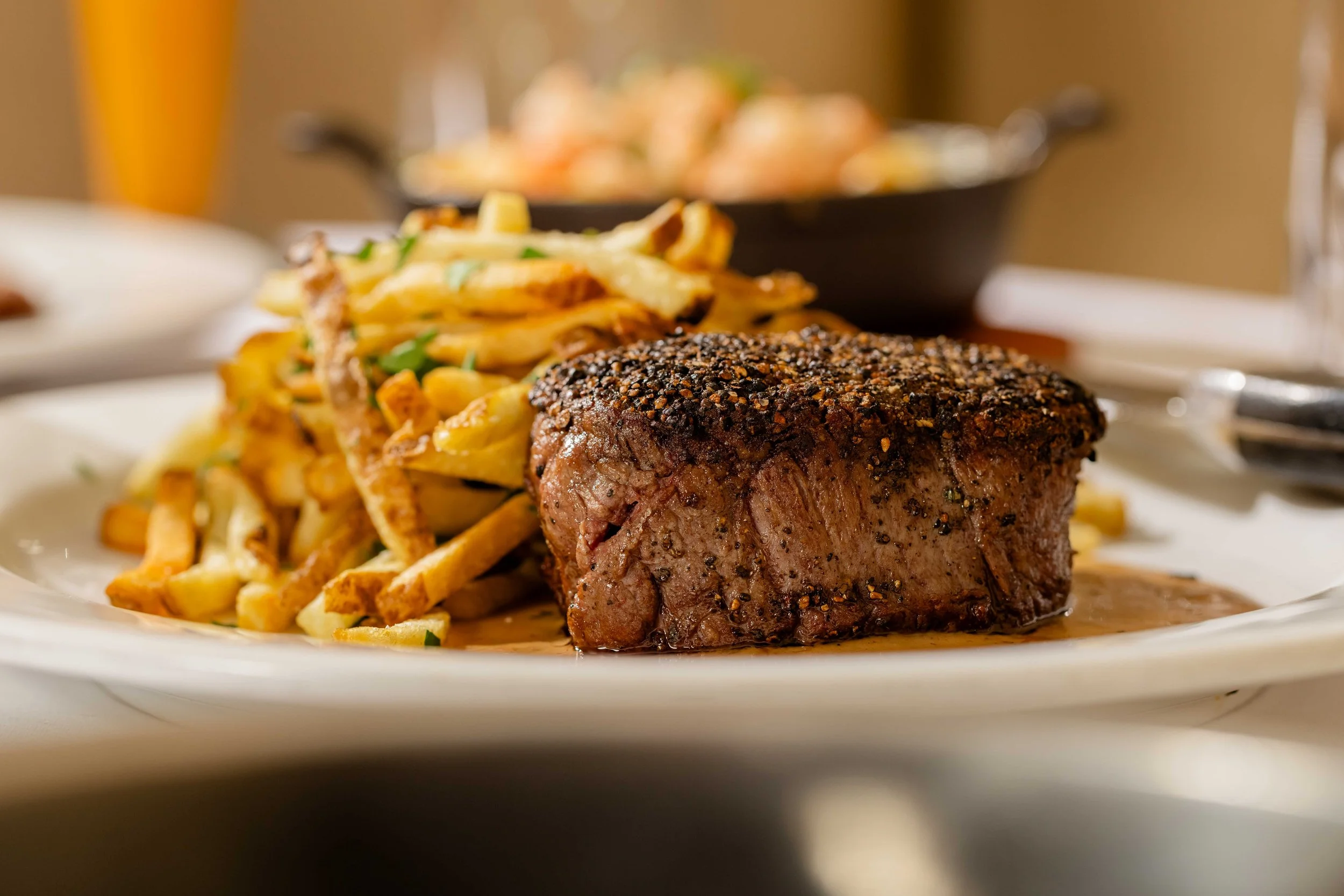 A plate of filet mignon prepared au poivre style topped with black pepper, served with a side of French fries with chopped green onions.