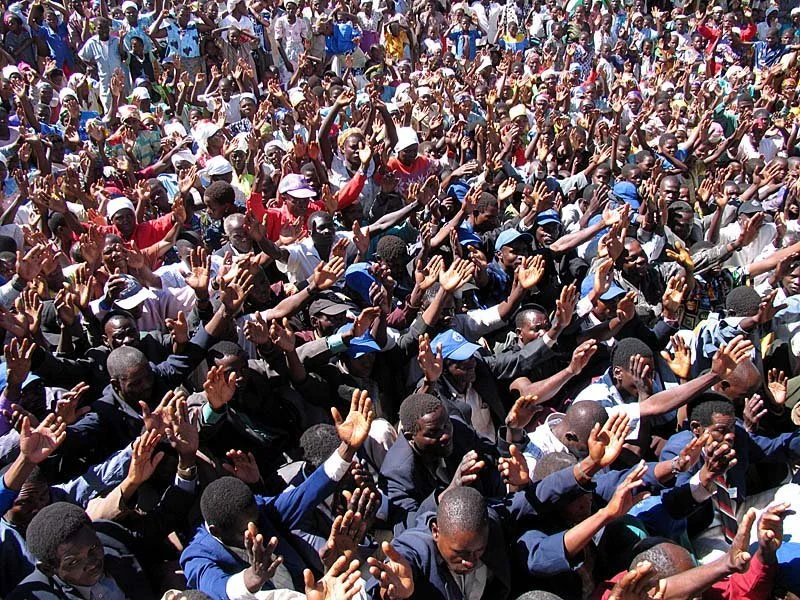 Pastors and their people in Malawi lifting their hands and hearts during a teaching session in the hot sun sitting in the dirt