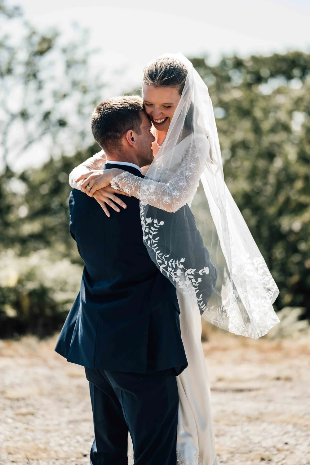 Groom lifting the bride as she laughs, veil catching the breeze