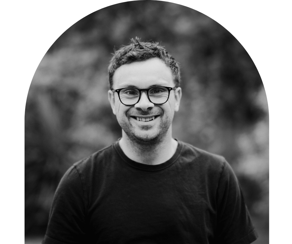 A smiling man with glasses and short hair outdoors.