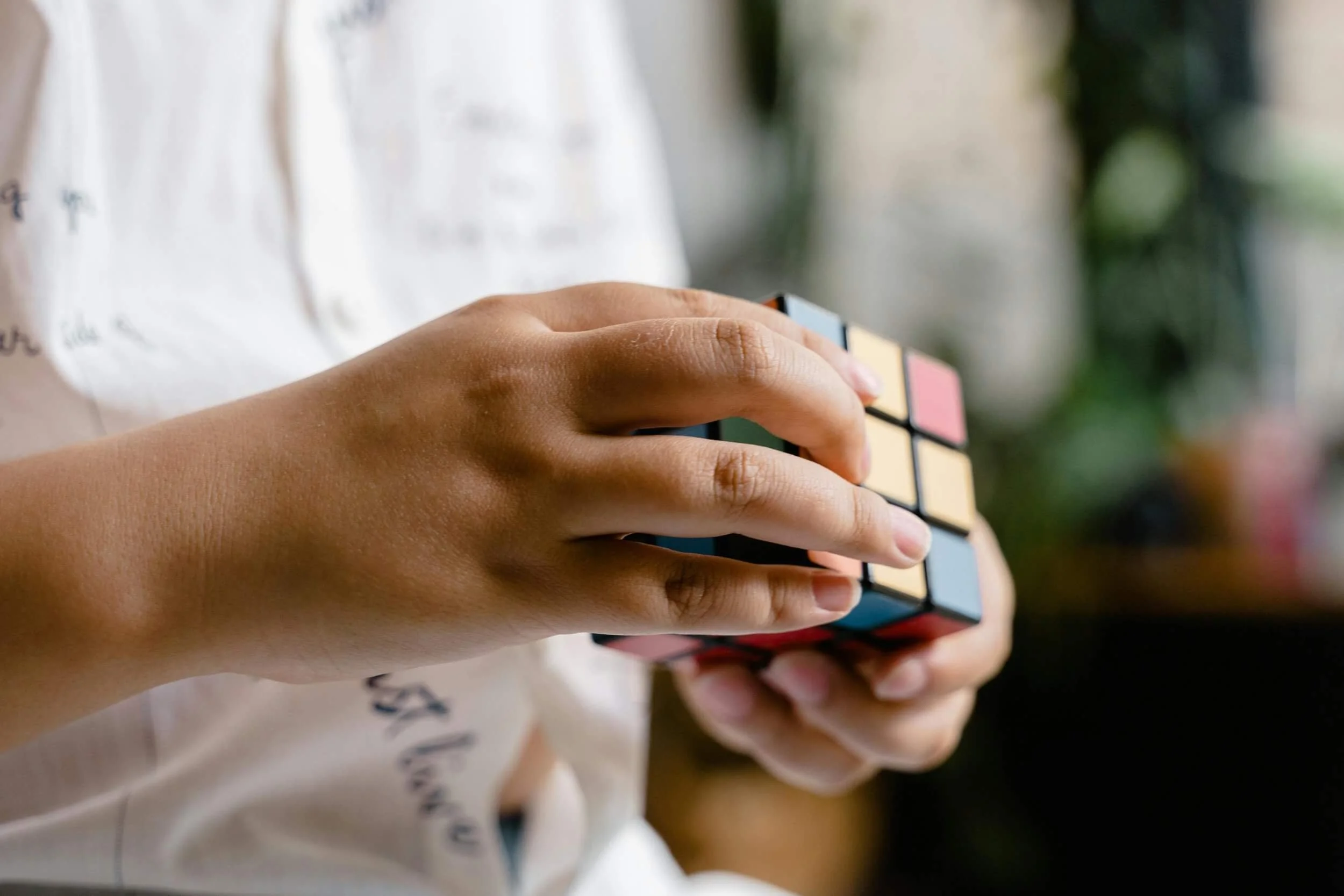 Close-up of a person’s hands manipulating a Rubik’s Cube with a soft focus background.