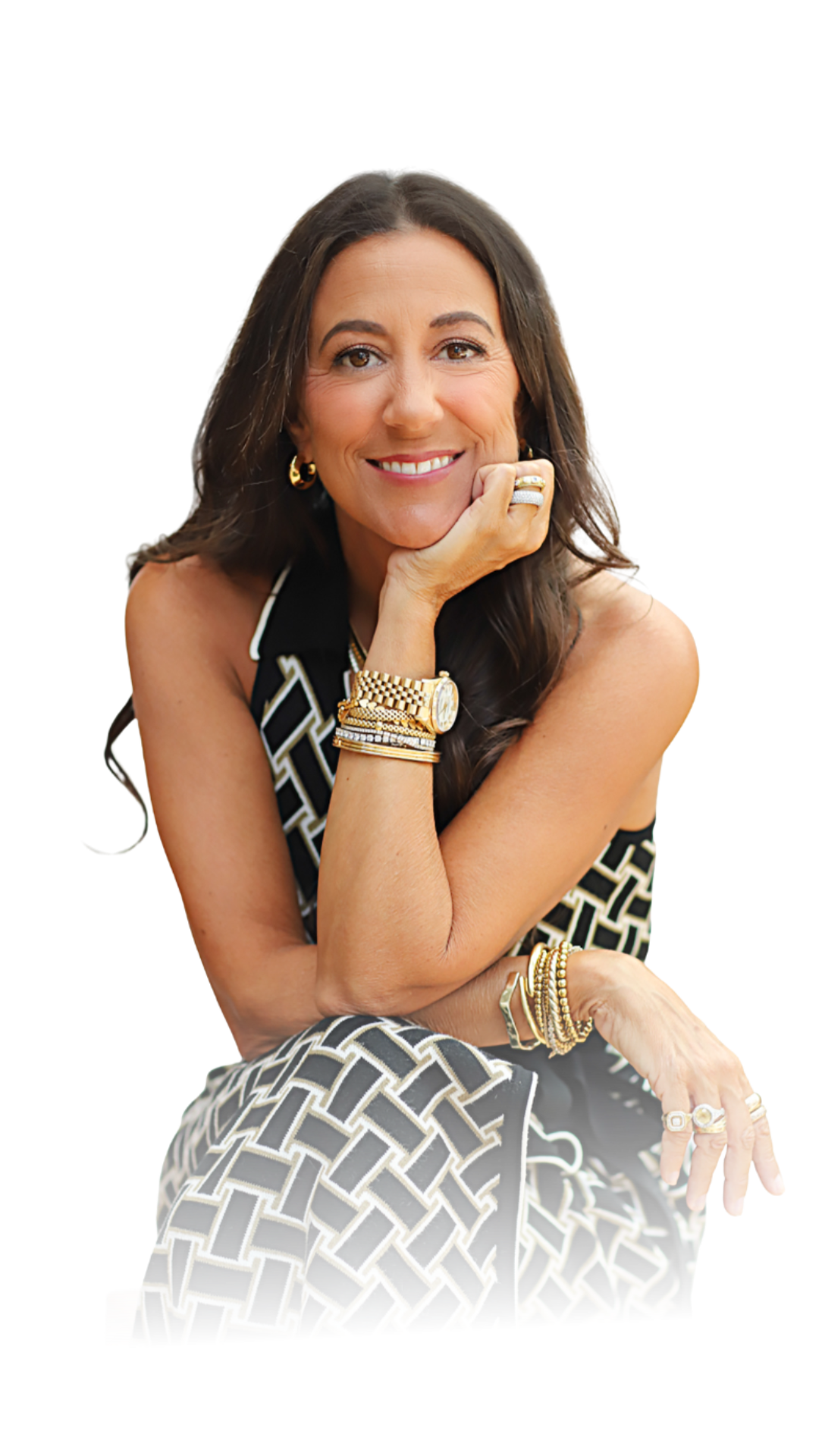 A woman with long dark hair, wearing a black and white patterned dress and gold jewelry, is smiling and resting her chin on her hand, sitting confidently.