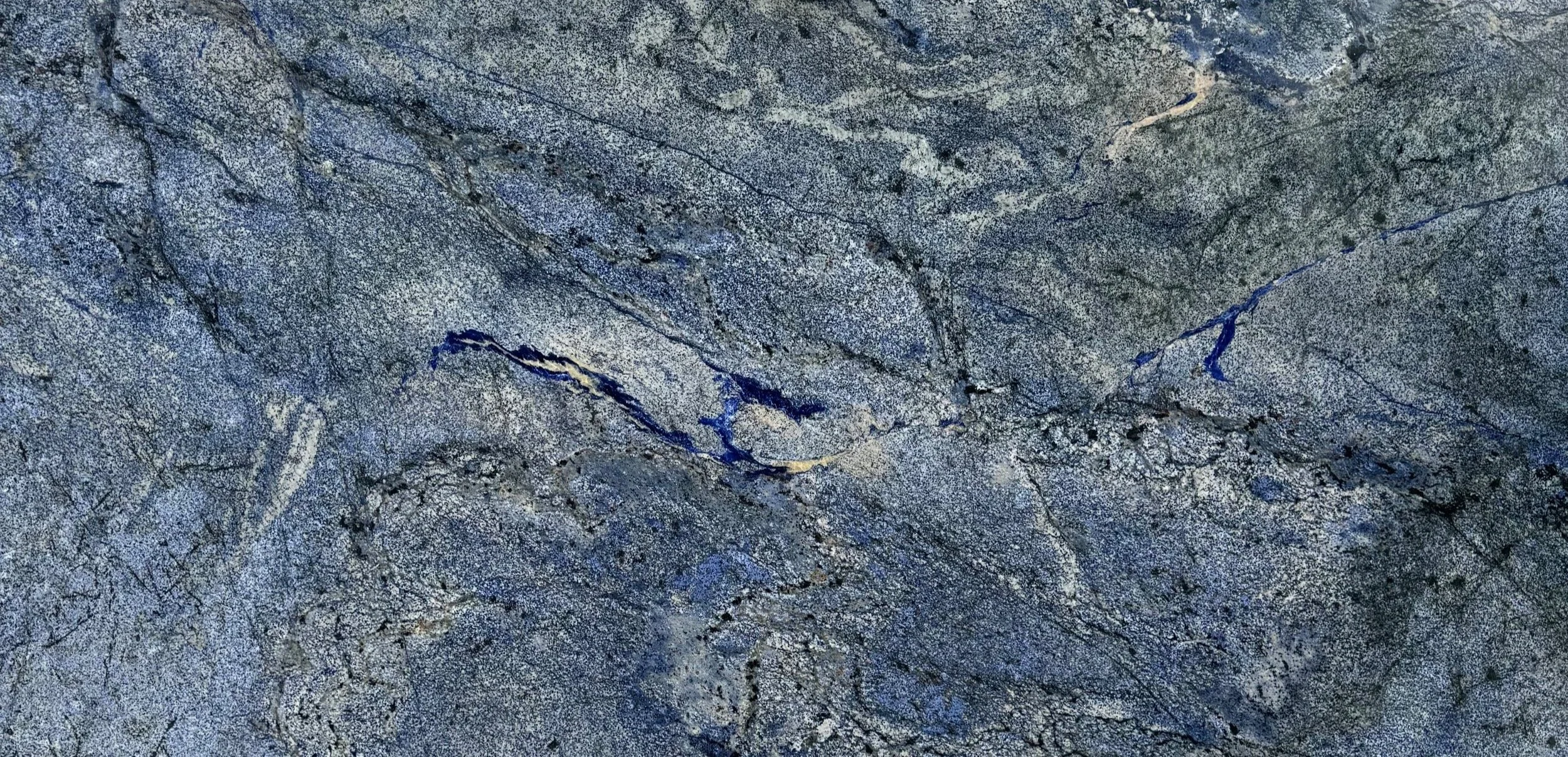 Close-up of a textured gray stone surface with blue and white veins and cracks.