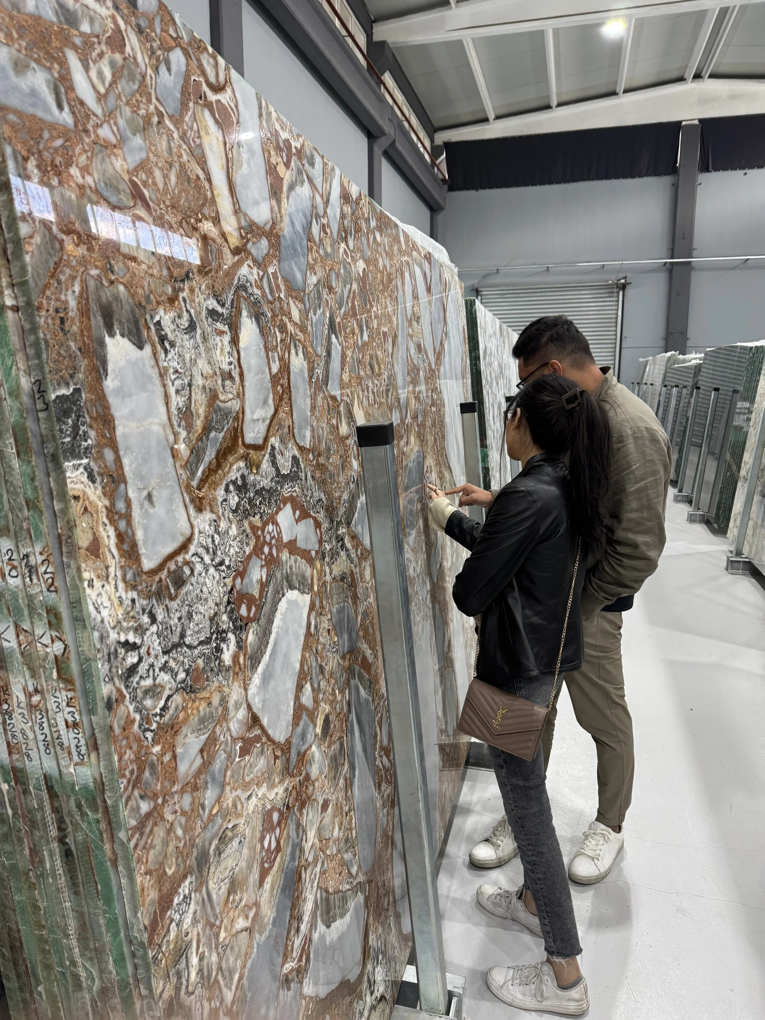 Two people shopping for large marble or stone tiles in a warehouse, looking at a display of patterned tiles.