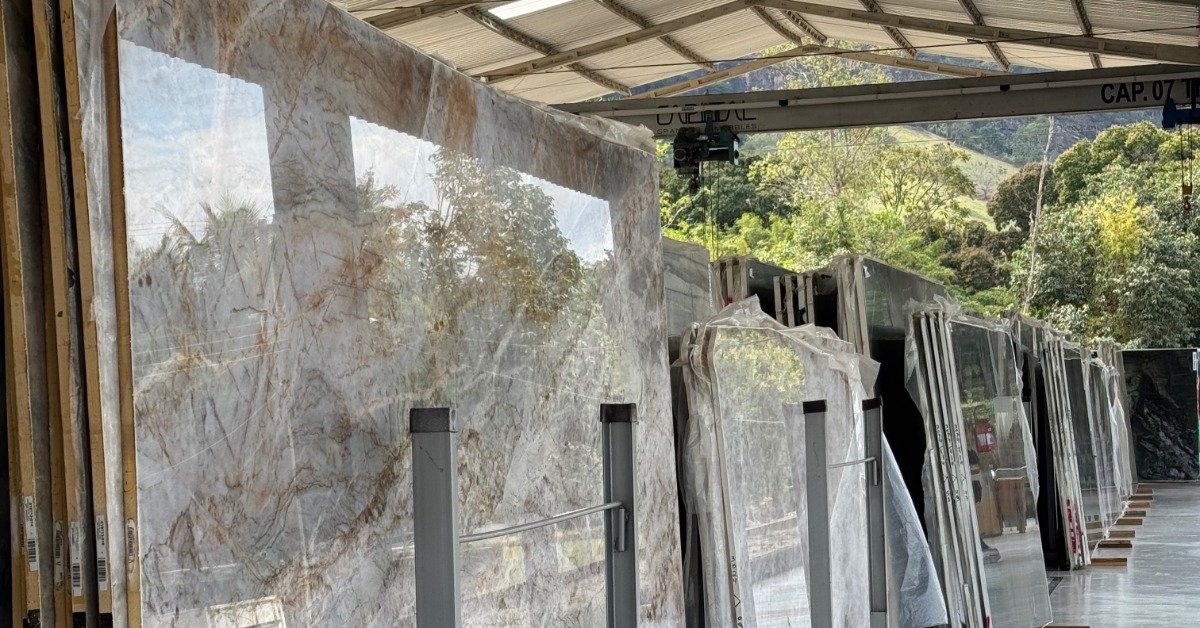 Polished stone slabs standing in rows under a covered structure, with trees and hills visible beyond the open sides.