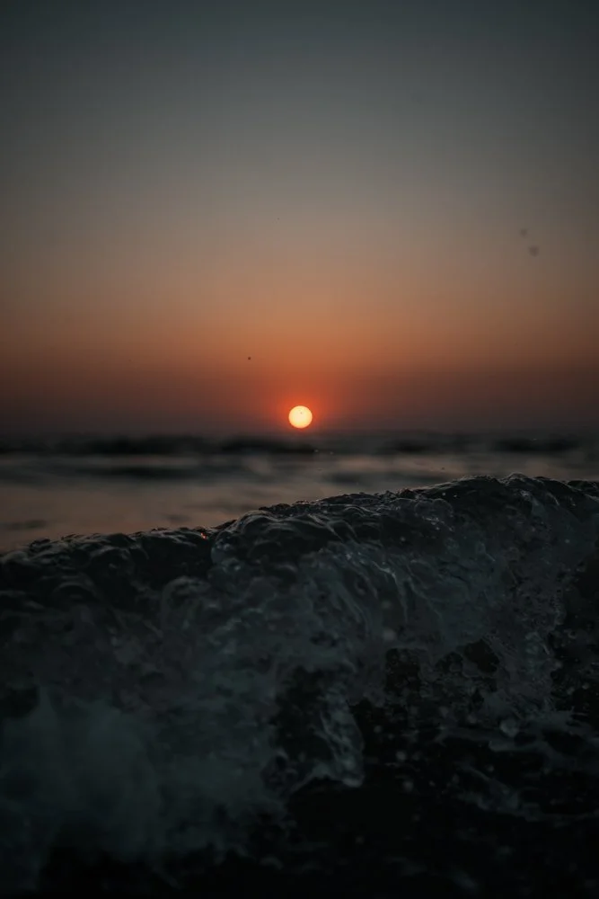 Sonnenuntergang über dem Meer mit Wellen im Vordergrund.