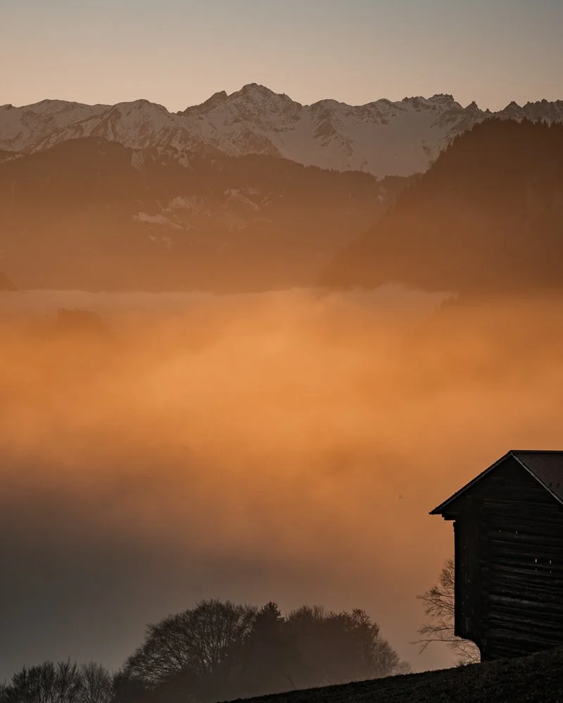 Berge im Hintergrund, Nebelmeer in der Mitte, dunkler Stall im Vordergrund.