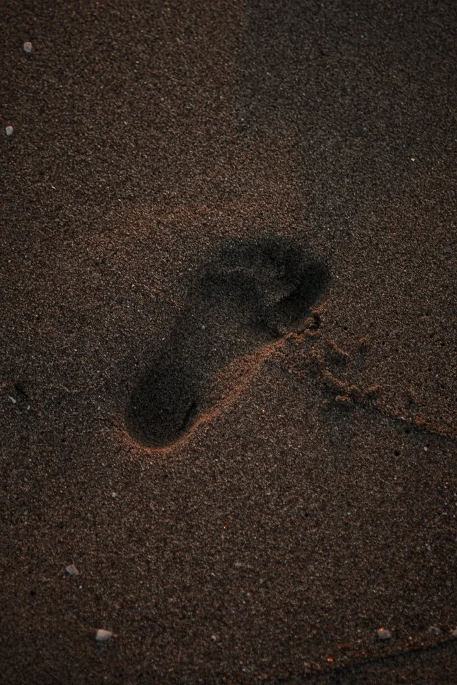 Fußabdruck im Sand auf einer dunklen, körnigen Oberfläche.