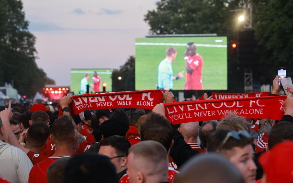 Spectateurs fans de football avec écharpes de Liverpool FC regardant un écran géant montrant un joueur et l'arbitre en conversation sur le terrain