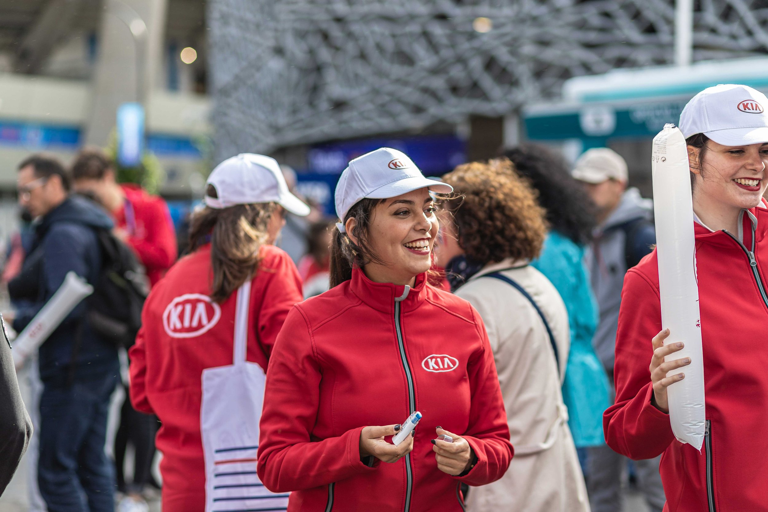 Groupe de personnes portant des vestes et des casquettes rouges avec logo Kia lors d'un événement en plein air.