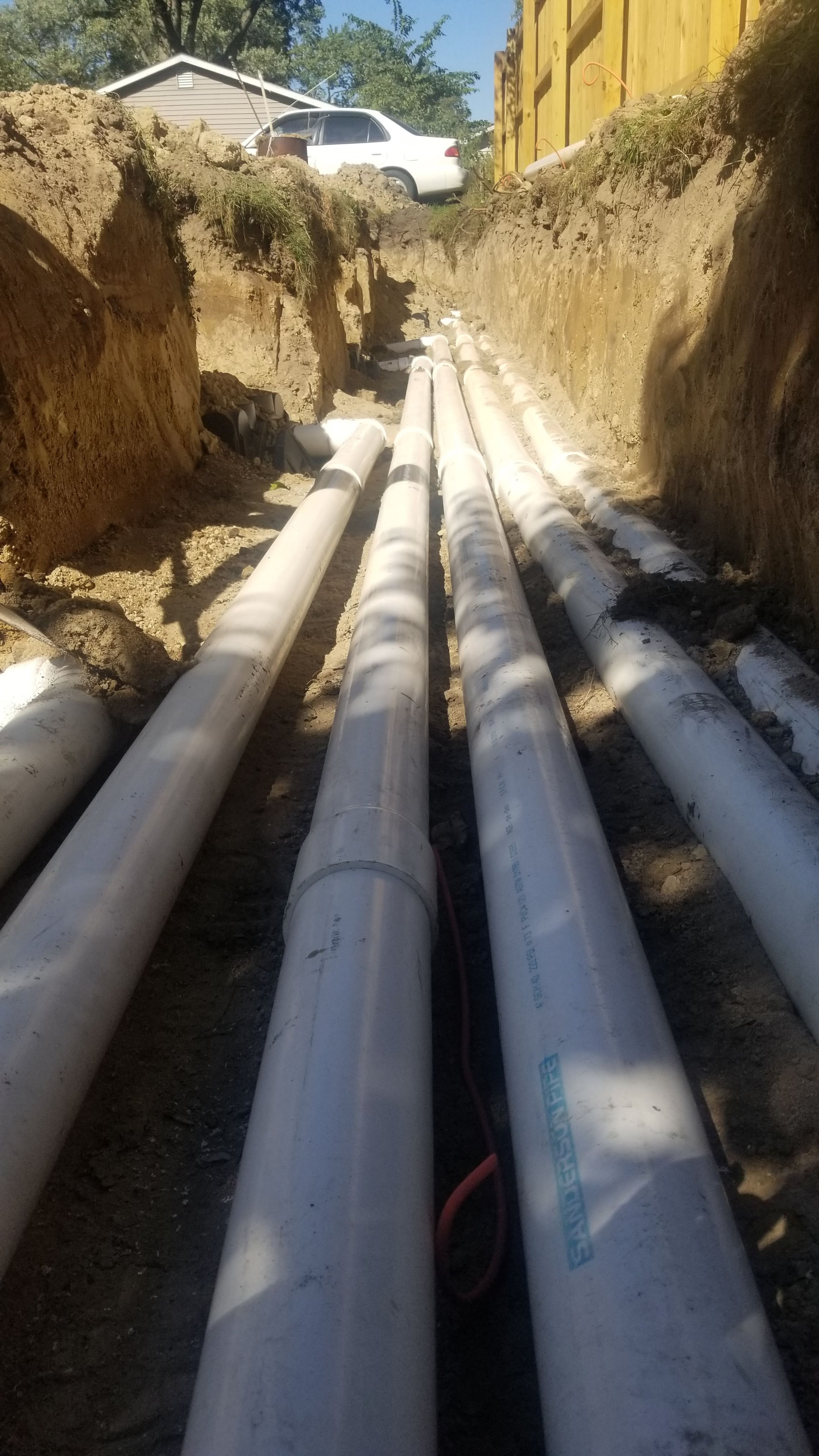 Underground water pipes being installed in a construction trench, with a house and a car in the background.
