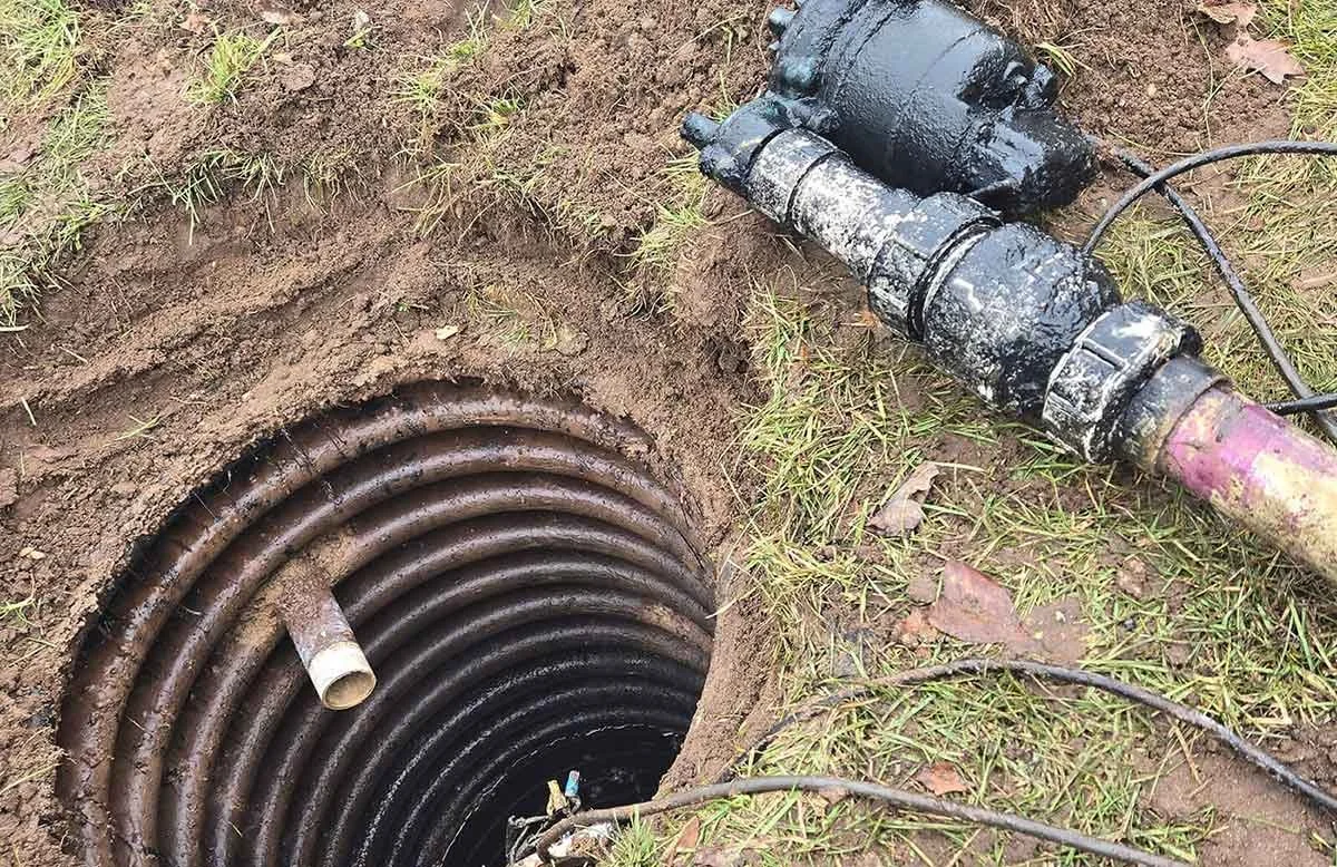 An open dirt hole with a coiled pipe inside and machinery nearby, outdoors.