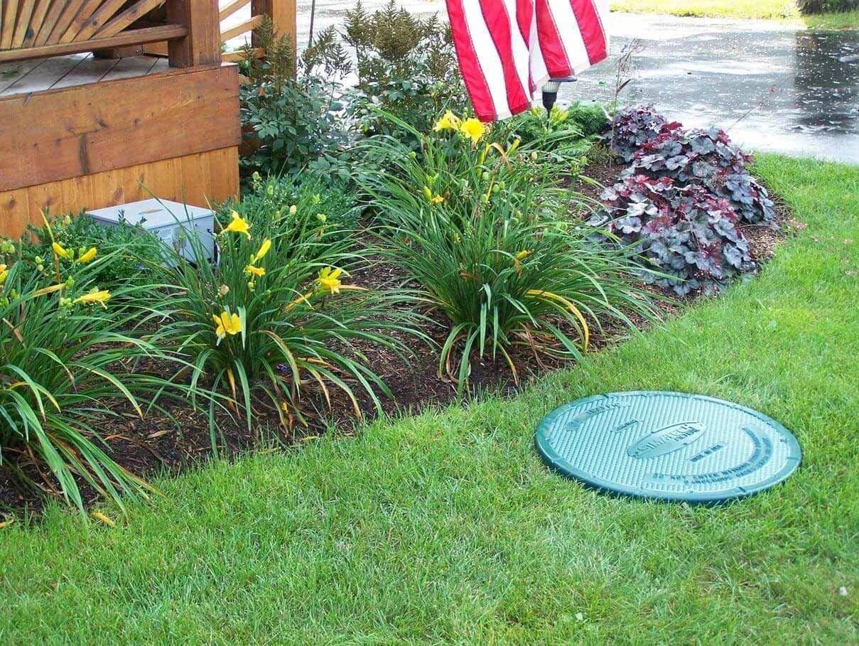 green septic tank lid visible in lawn near landscaped garden bed