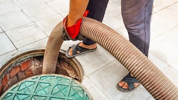 A person using a large vacuum hose to clean out a sewer or drainage system on a city sidewalk.
