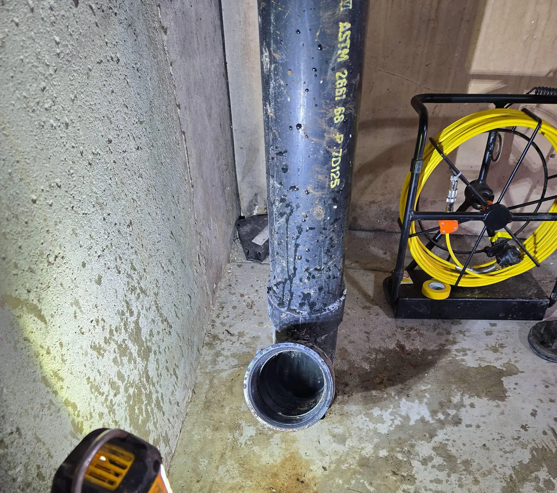 Clean black pipe on the floor of a construction site or basement with yellow coiled extension cord on a black cart nearby.