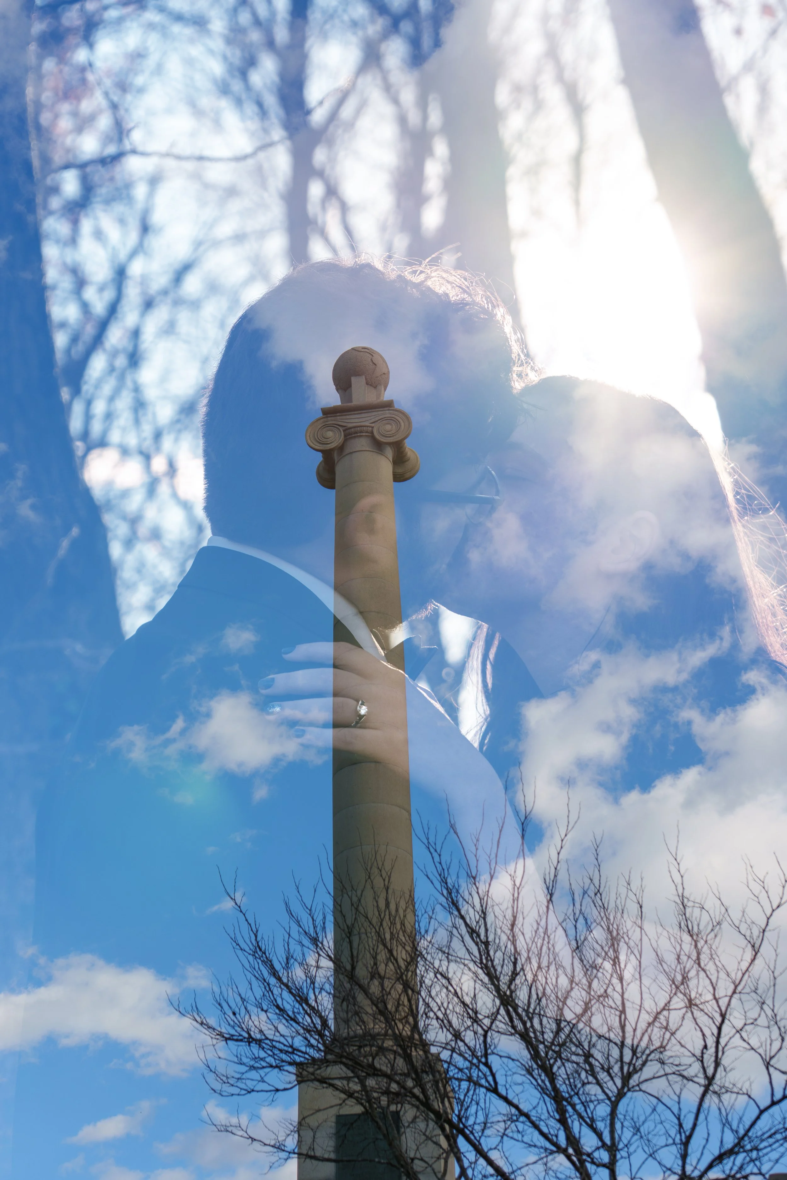 Double exposure photo of a man and a woman with a column and a blue sky with clouds and bare tree branches.