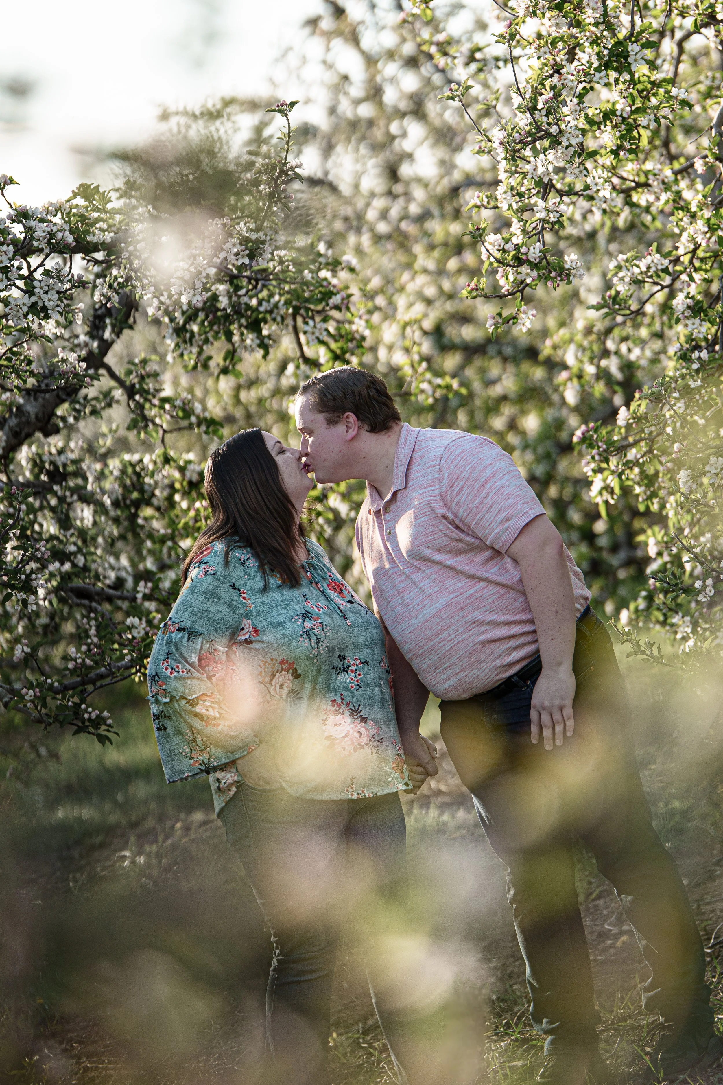 A couple sharing a kiss outdoors among blossoming trees during daytime.
