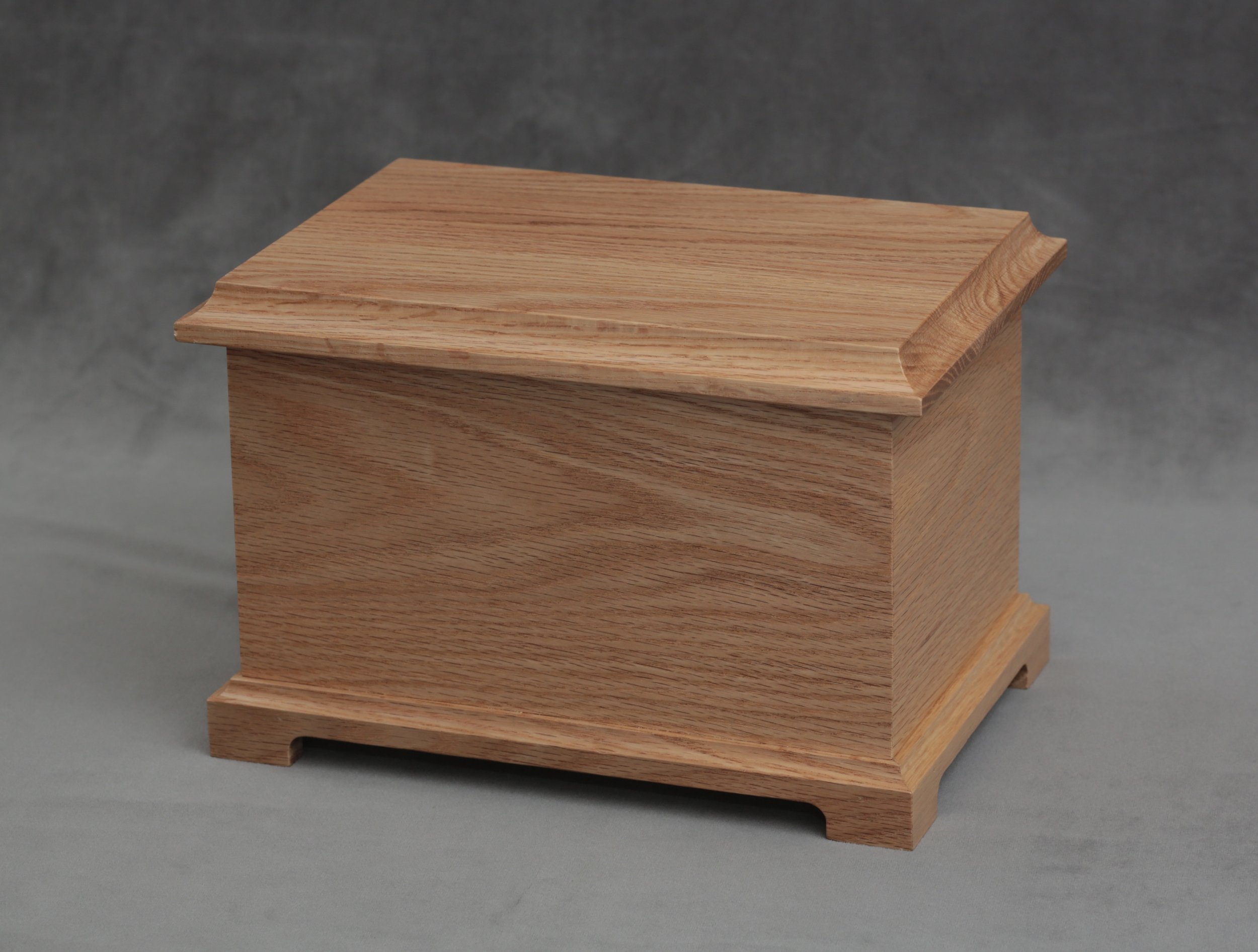Wooden funeral urn with a smooth, polished surface and a slightly curved lid, set against a dark gray background.
