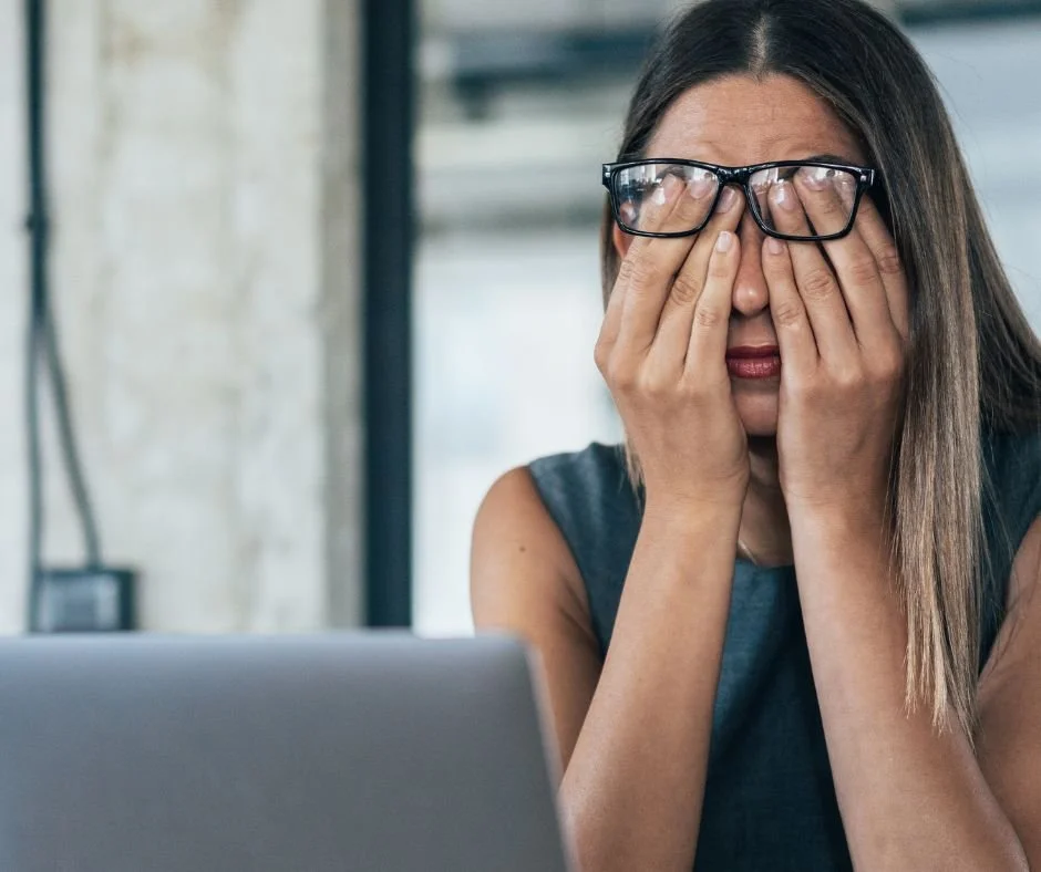 Stressed out woman in front of laptop rubbing her eyes.