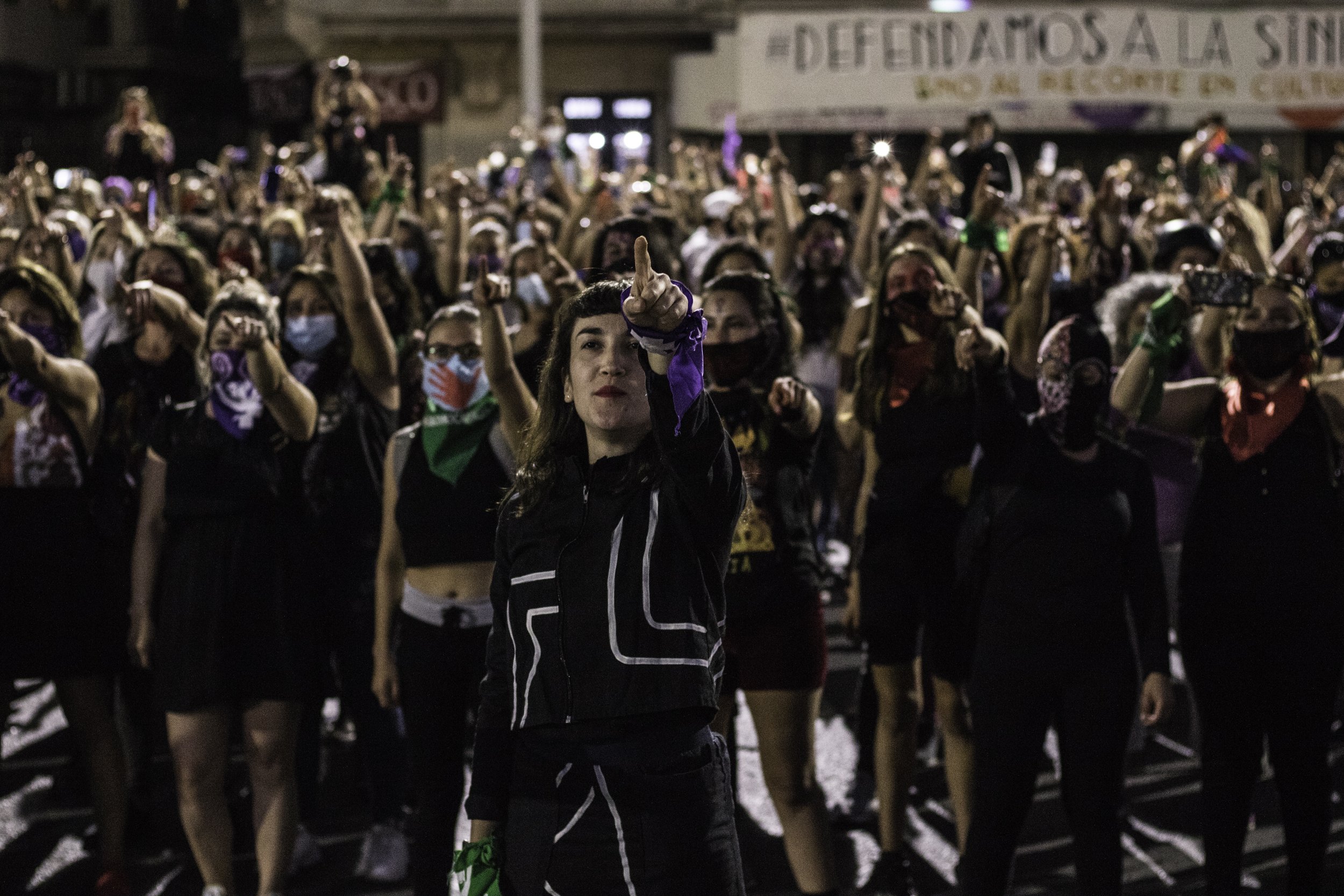 Group of protest performers stand facing the camera with their arms raised and fingers pointing forwards