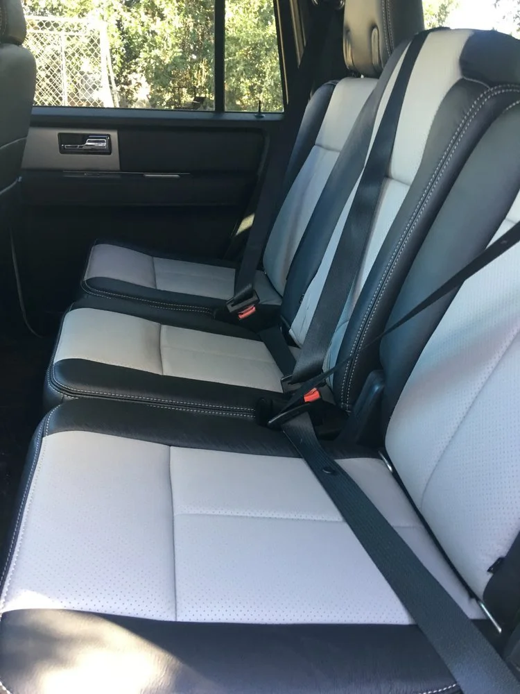 The backseat interior of a vehicle with black and white upholstered seats and black seat belts.